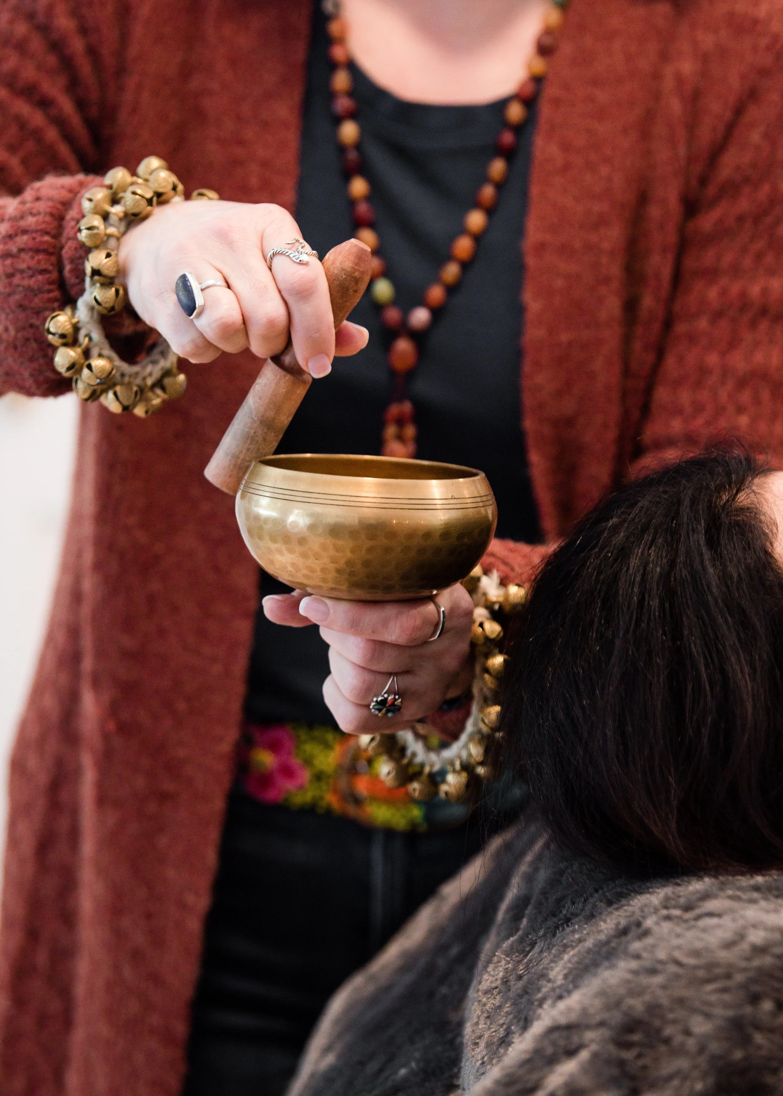 A person wearing jewelry is using a mallet to strike a Tibetan singing bowl held in another person’s hand.