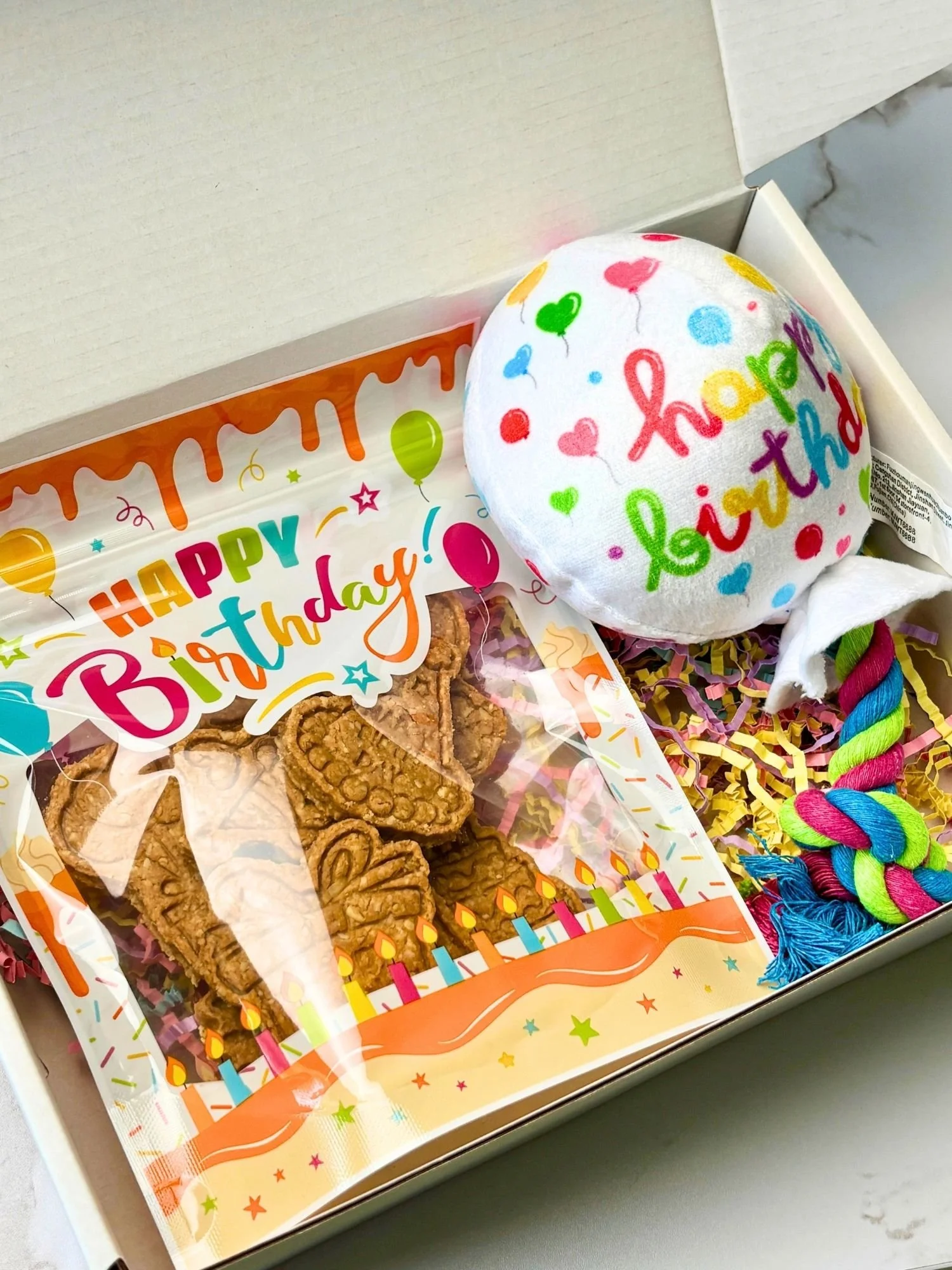 Dog birthday gift box with birthday-stamped treats and squeaky balloon rope toy
