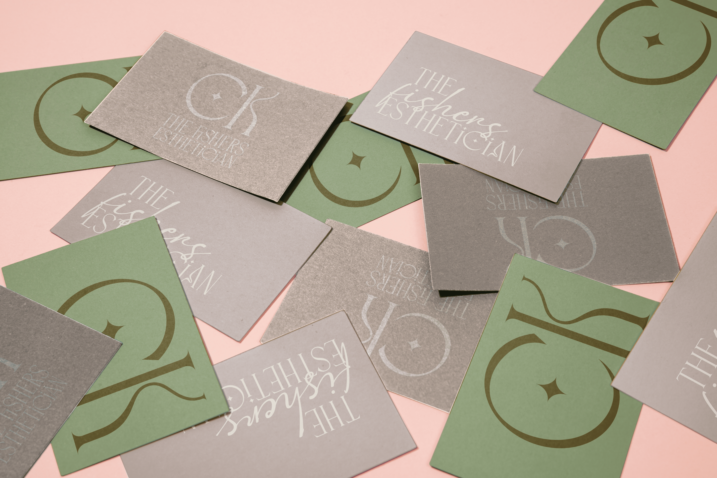 A collection of business cards and paper squares with a pastel pink and green background. The cards have a minimalist design with white text and a star and moon motif, featuring the words "THE FISHER'S AESTHETICIAN".