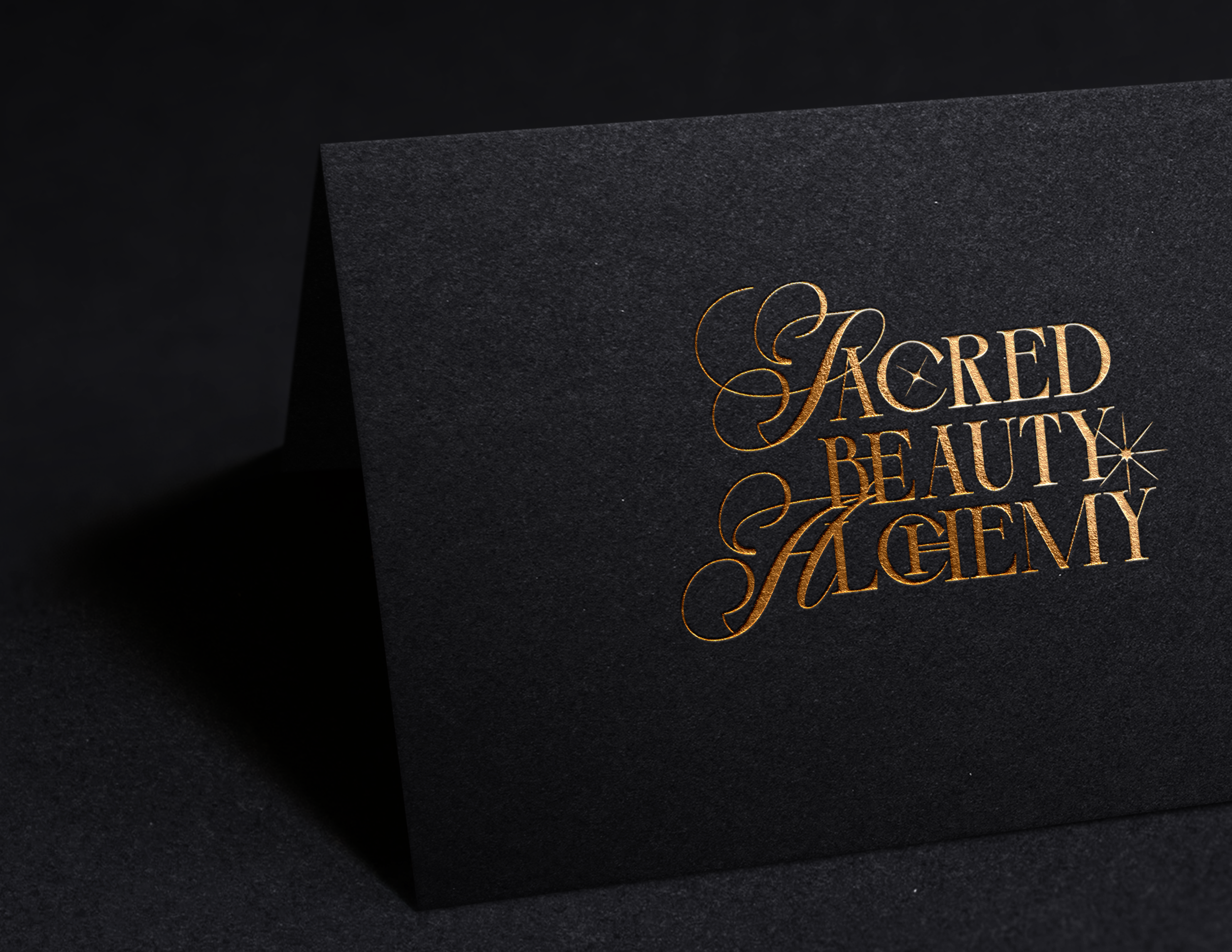 Close-up of black textured paper with the words "Sacred Beauty & Gallery" in elegant gold lettering.