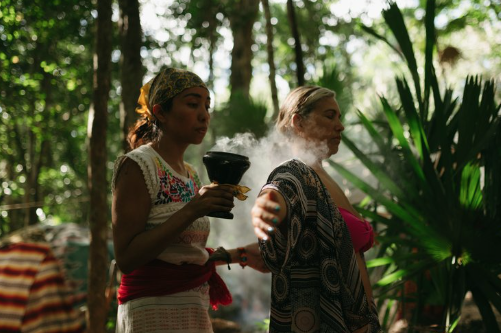 Two women in a forest performing a smoke cleansing ritual.