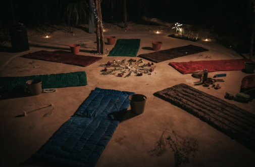 Candlelit setting with mats in a circle, surrounded by plants and small objects.