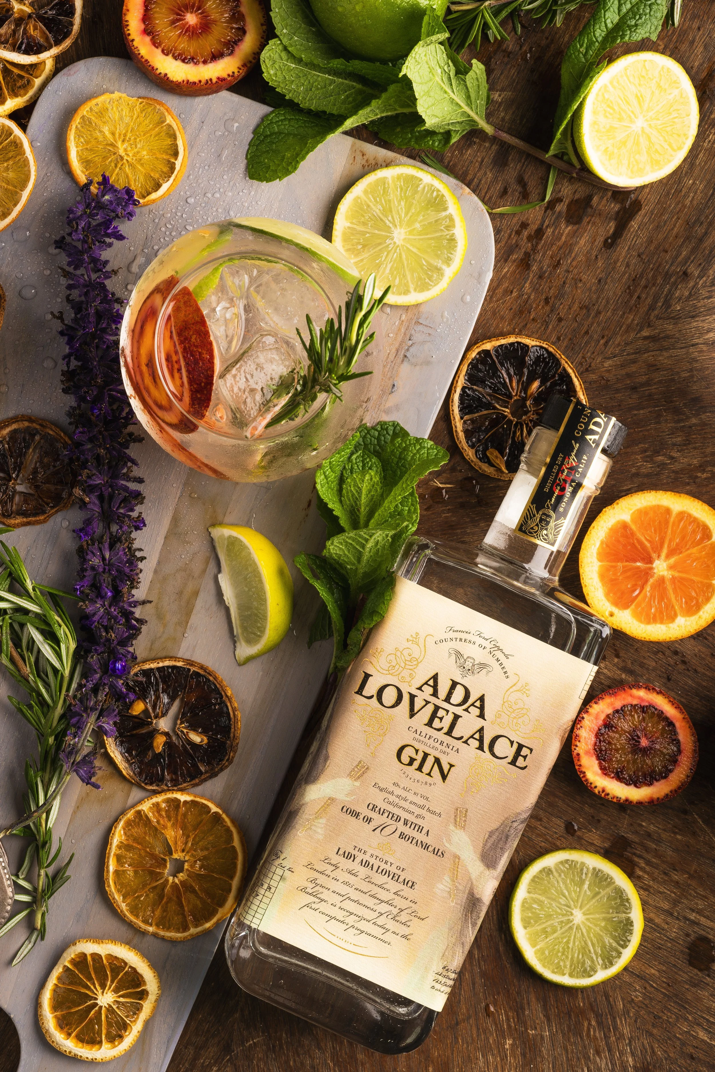 Flat lay of Ada Lovelace Gin Bottle and a vibrant array of fresh and dried citrus with a gin and tonic. There are fresh herbs scattered in the flat lay in a very systematic but random layout.  XÔL CREATIVE IS A BAY AREA CALIFORNIA PRODUCT AND FOOD PH
