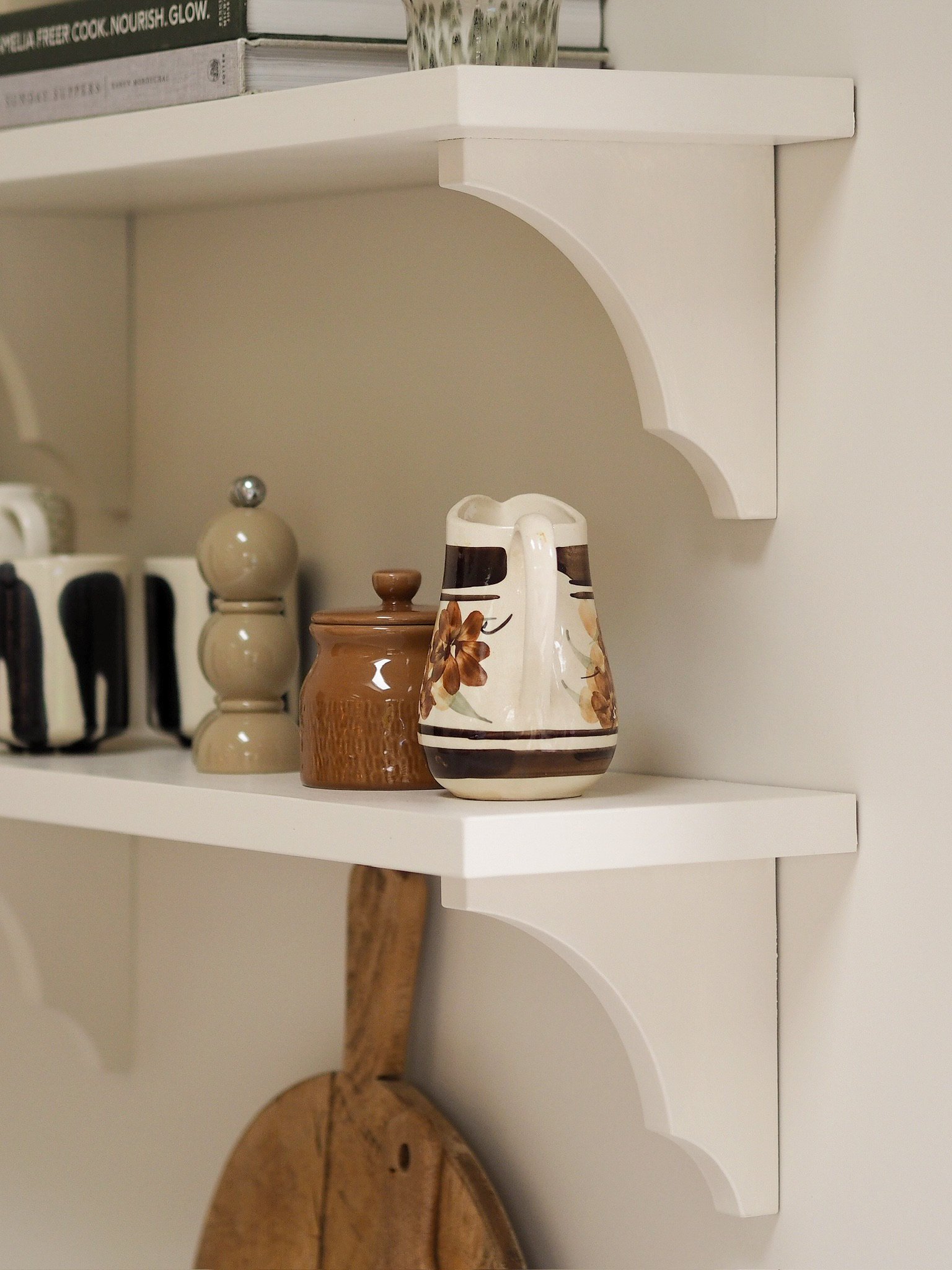 White wall shelf with three decorative vases and additional items, with a wooden object below.