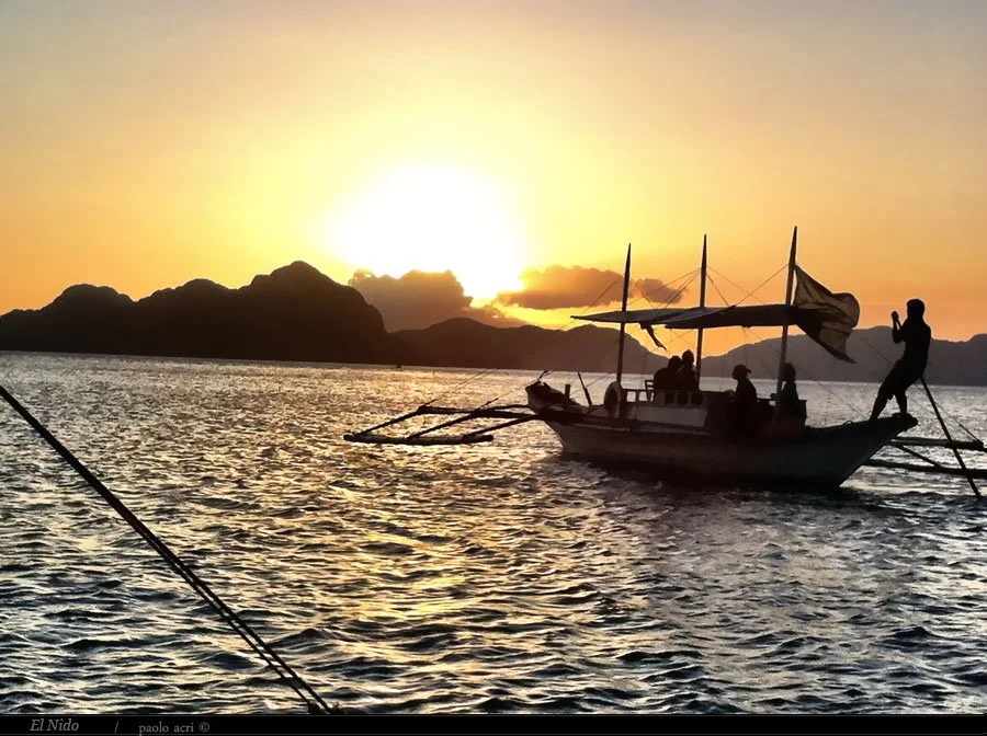 Silhouetted boat with people at sunset on the water, with mountains in the background.