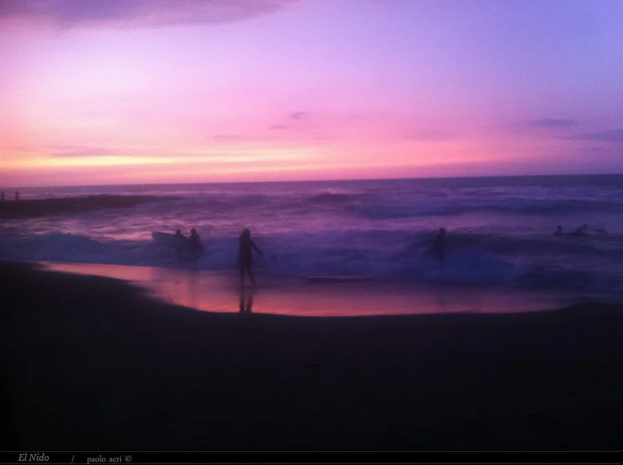 People on the beach during sunset with a colorful sky in shades of pink, purple, and yellow.
