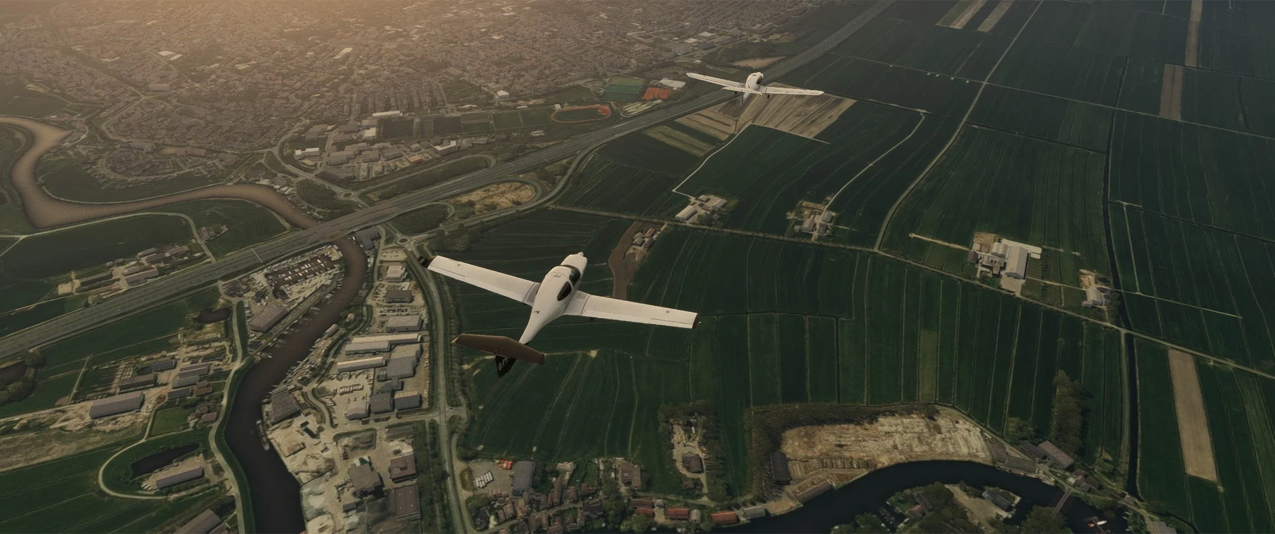 Two small white aircraft flying over green fields, rivers, roads, and buildings.