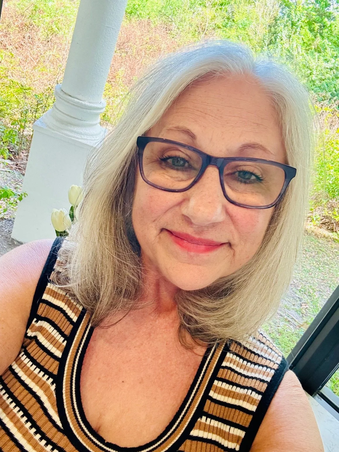 Lisa Assetta smiling warmly, with greenery and white pillars in the background