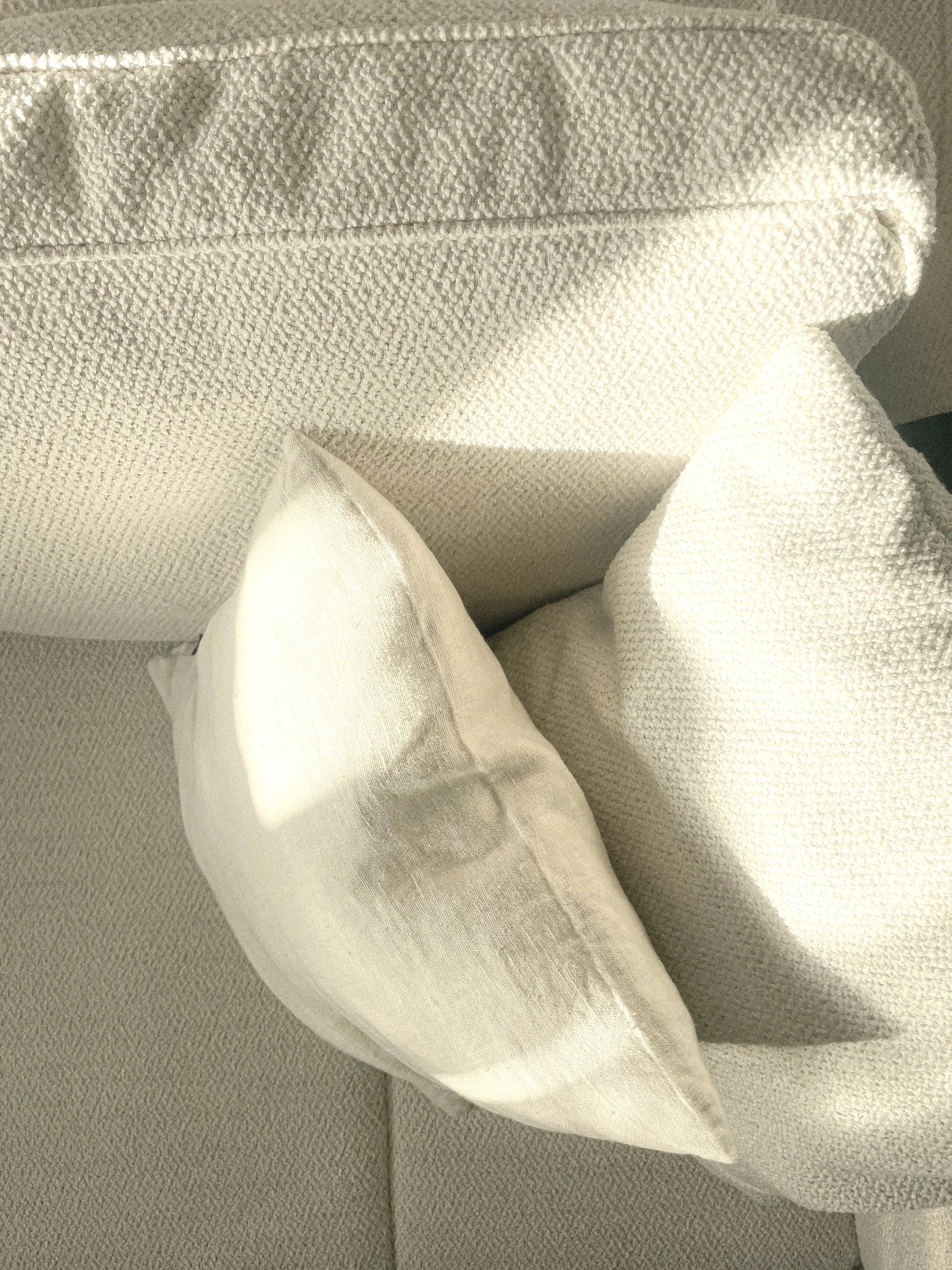 A close-up of a white or cream-colored textured fabric sofa with a matching decorative pillow and a blanket or drape of the same fabric.Residential interior design project in Scotland - Interior Designer Scotland - Interiors 