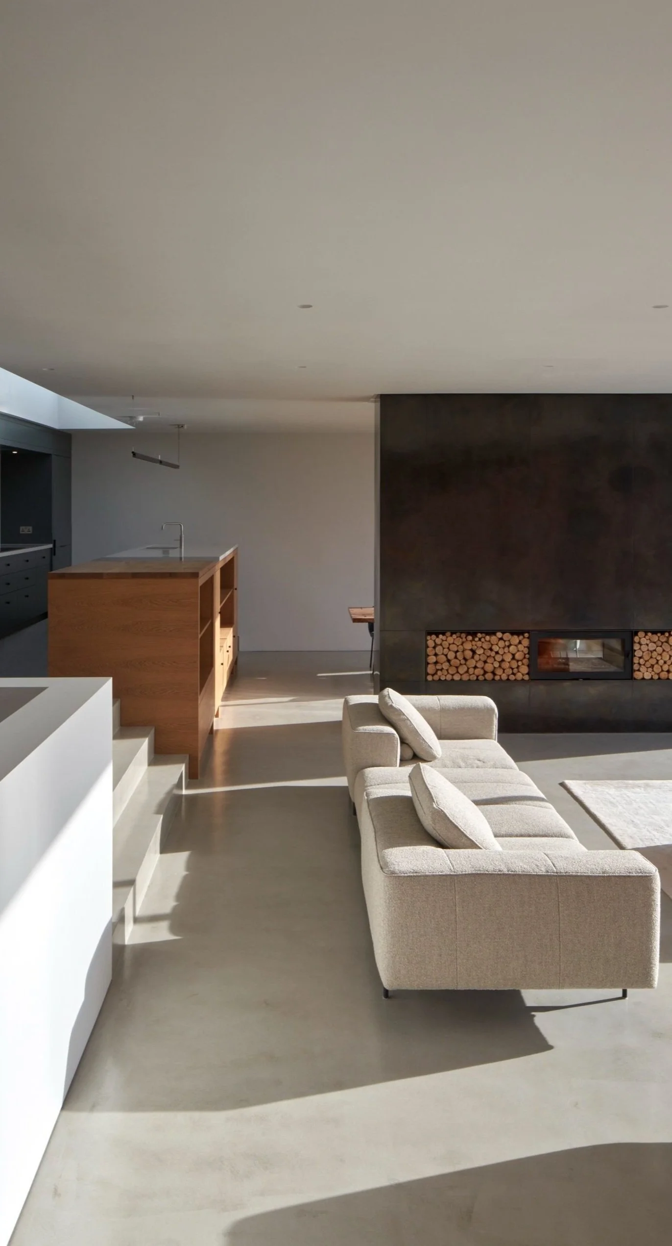 Modern living room with a beige sofa, black fireplace with stacked logs, and minimalist kitchen with wooden island.“Residential interior design project in Scotland by [Studio Name], working across Glasgow, Edinburgh, Dundee and the Highlands.”

“Cont