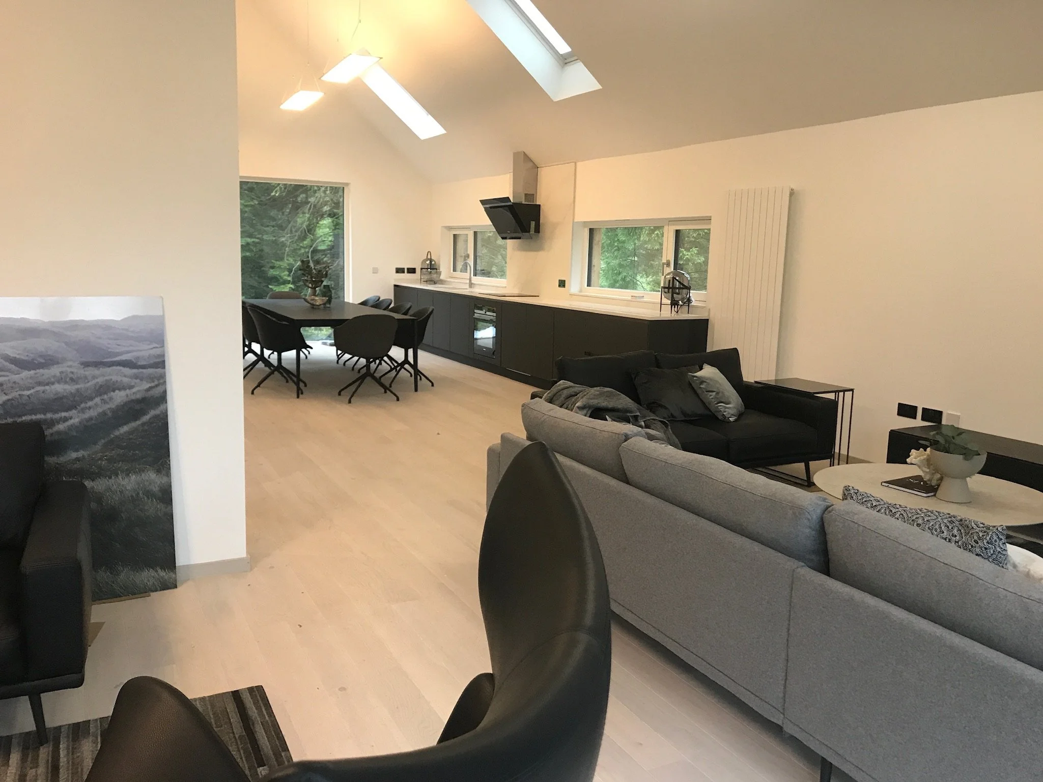 Modern open-plan living area with a dining table, kitchen, and sofas, featuring skylights and large windows with greenery outside.Residential interior design project in Scotland - Interior Designer Scotland - Interiors 