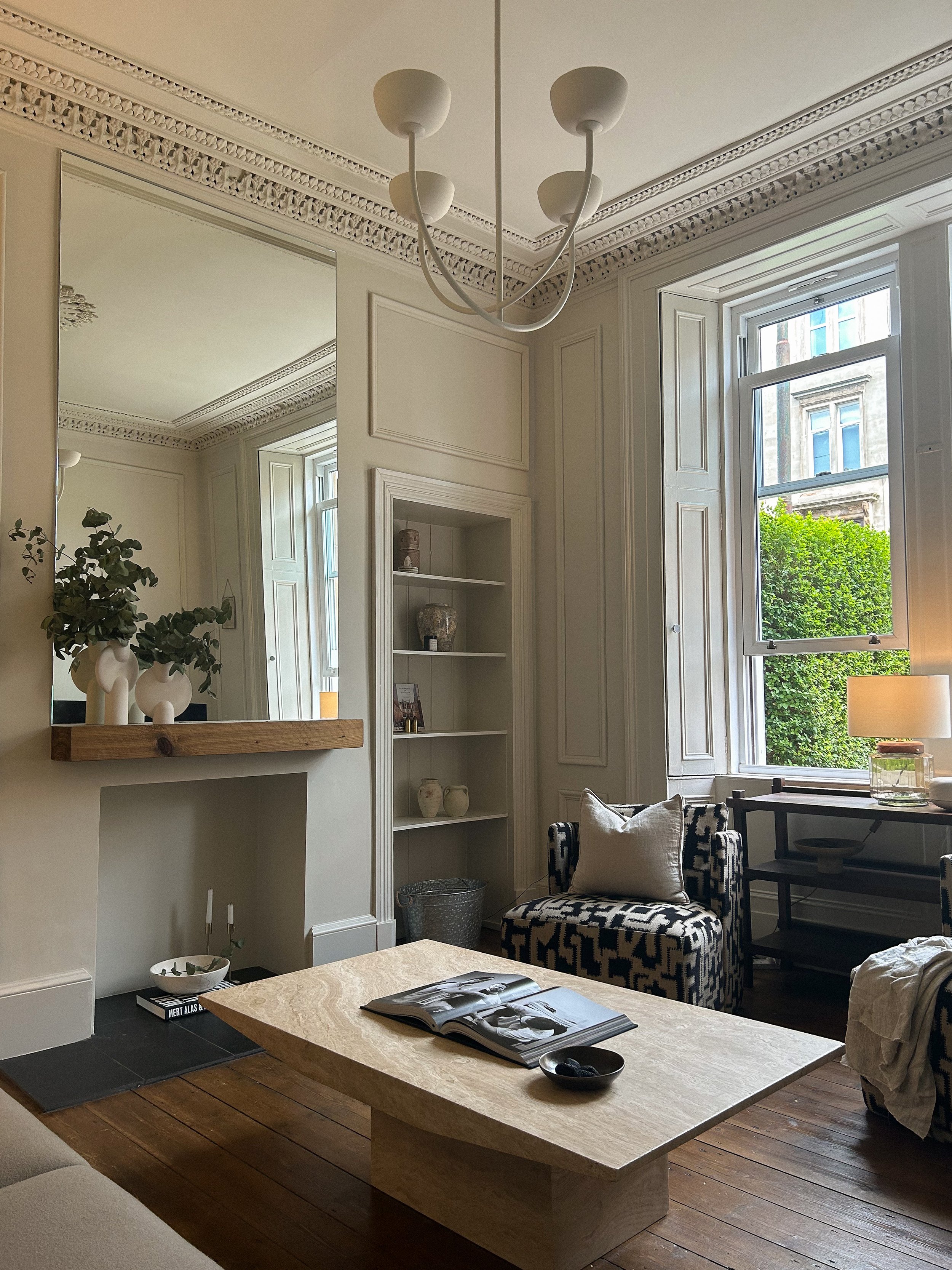 Living room with a fireplace, built-in bookshelf, large window, armchair, table with magazine, and decorative vases on a ledge.Residential interior design project in Scotland - Interior Designer Scotland - Interiors 