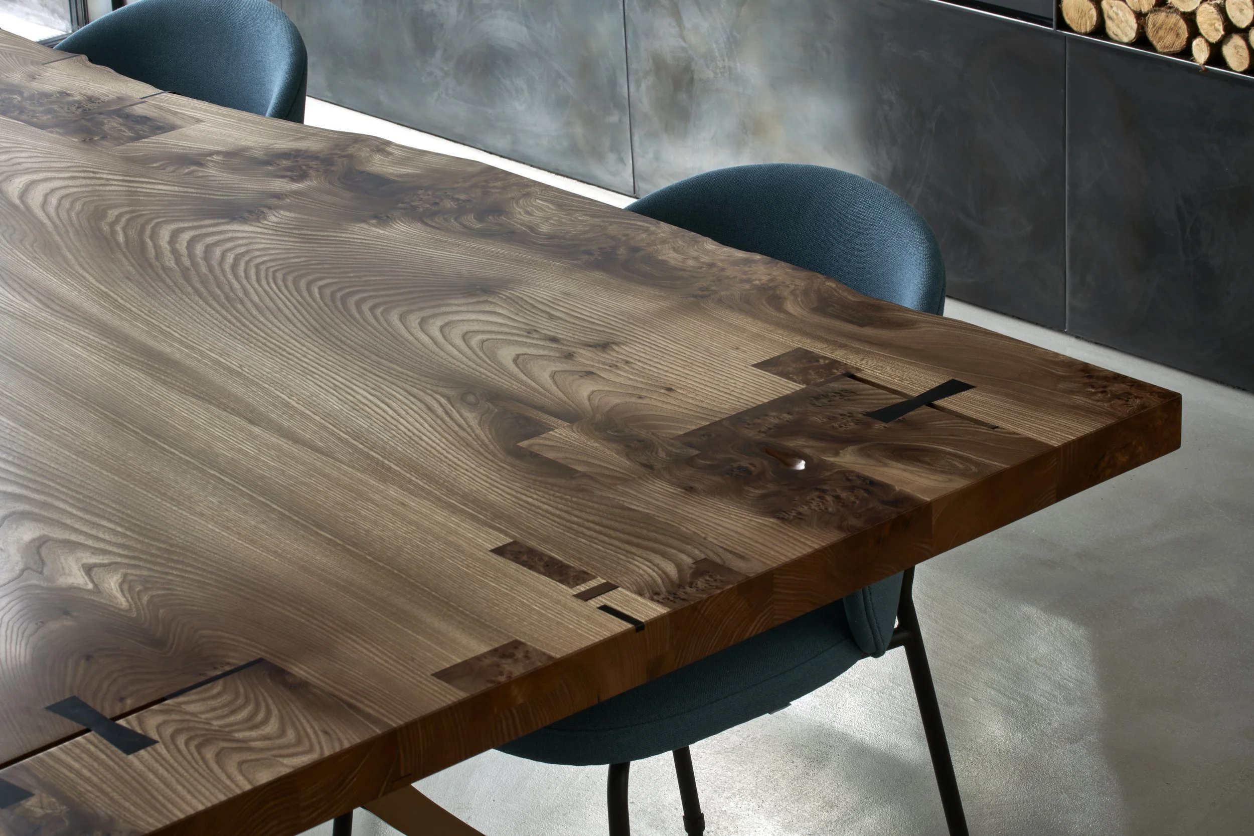 Close-up of a large wooden table with a natural wood grain pattern and black inlay accents, surrounded by teal upholstered chairs in a modern interior setting.“Residential interior design project in Scotland - Interior Designer Scotland - Interiors 