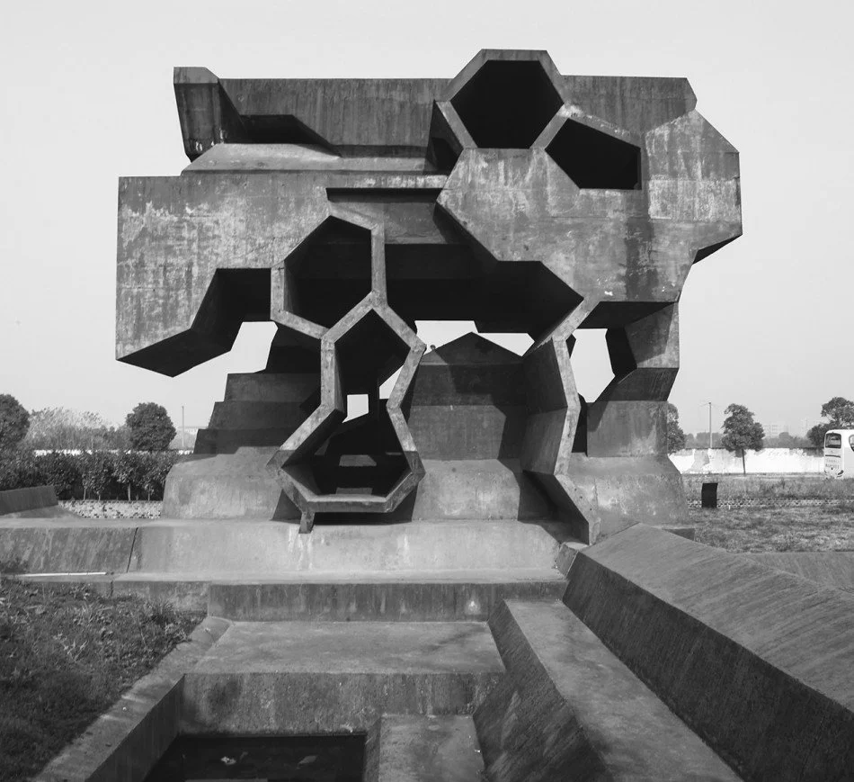 Concrete sculpture of a lion's head with geometric, honeycomb-like openings, situated outdoors with trees and a bus in the background.Residential interior design project in Scotland - Interior Designer Scotland - Interiors 