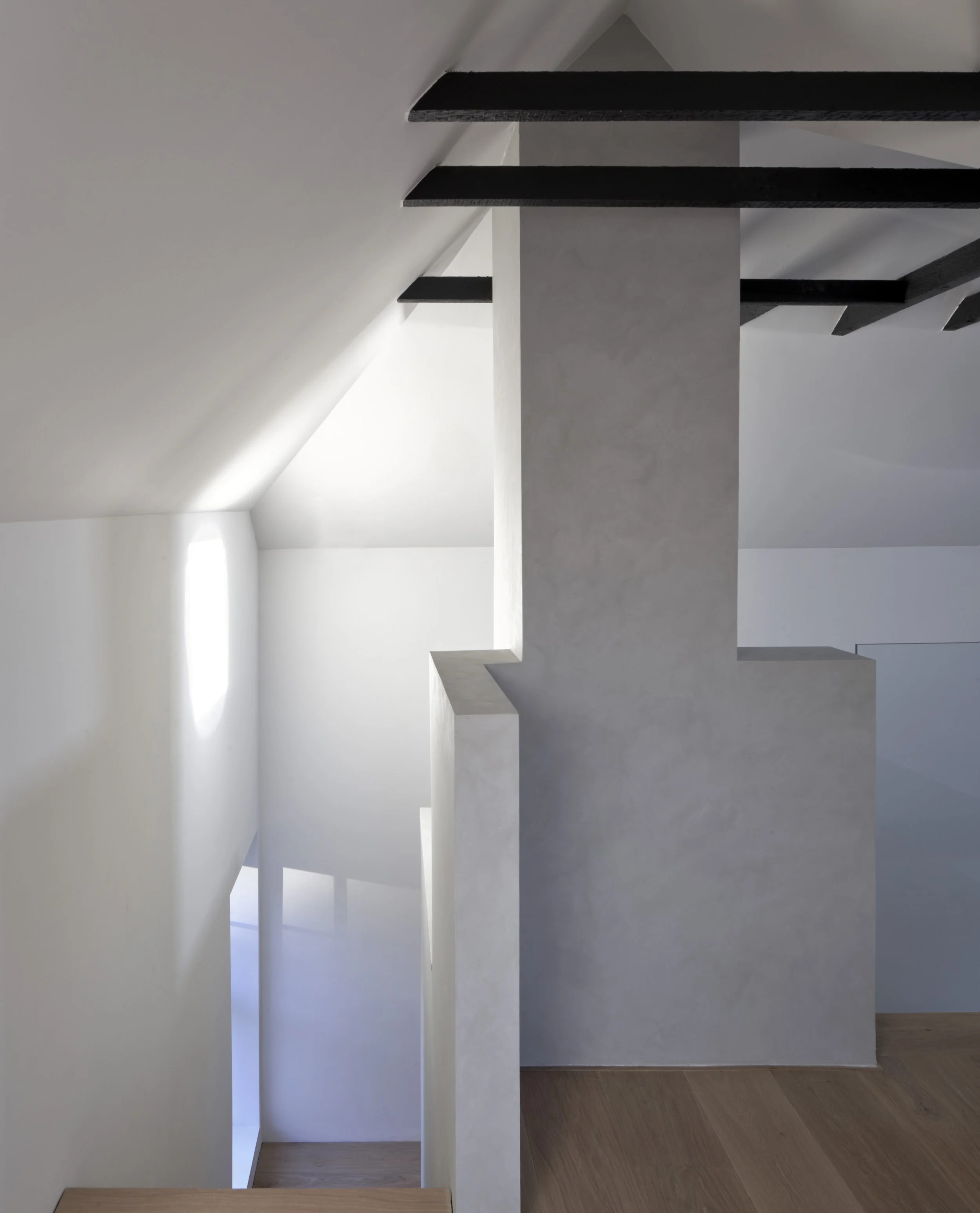 Interior view of a modern staircase with dark wooden steps, a white inclined wall, and a textured concrete pillar, with sunlight streaming through a window.Residential interior design project in Scotland - Interior Designer Scotland - Interiors 
