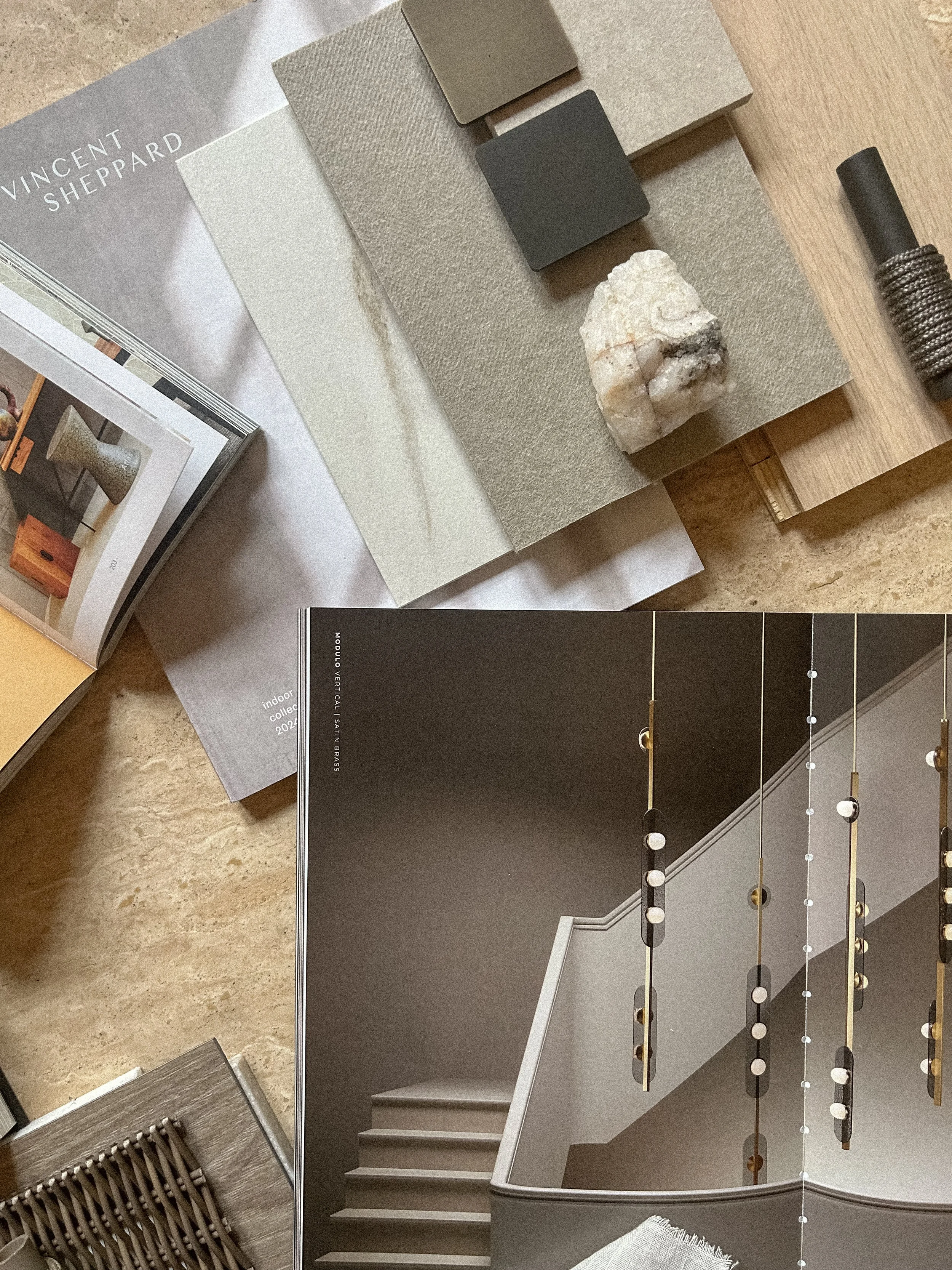 A collection of interior design samples and materials, including fabric swatches, stone pieces, color tiles, a lighting fixture, and a design magazine, arranged on a wooden surface.Residential interior design project in Scotland - Interior Designer S