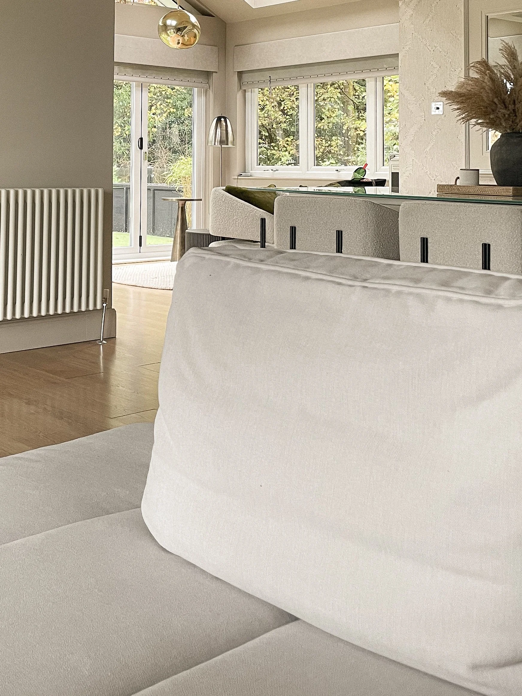 A modern living room with white couches, wooden flooring, large windows, and outdoor greenery visible through the windows and sliding door.“Residential interior design project in Scotland by [Studio Name], working across Glasgow, Edinburgh, Dundee an