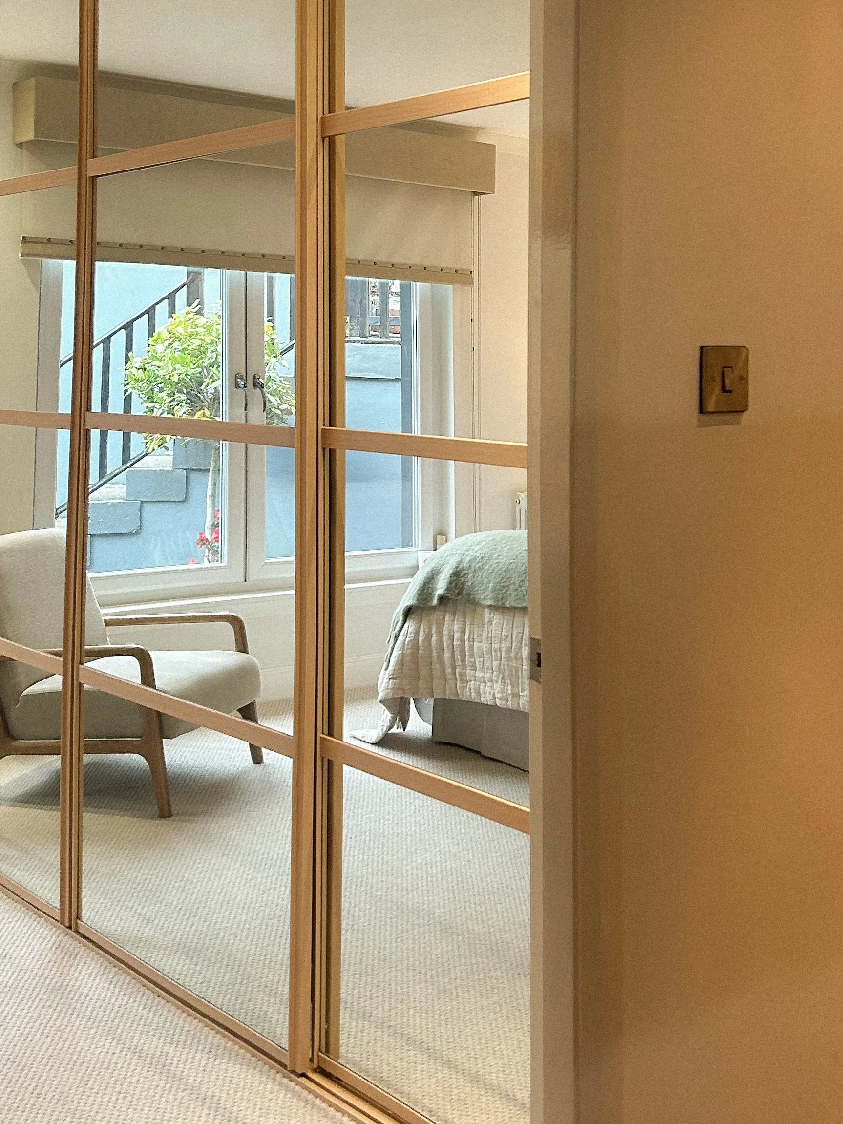 Interior view of a bedroom with a bed, a chair, and large window with greenery outside, seen through glass sliding doors with a wooden frame.“Residential interior design project in Scotland by [Studio Name], working across Glasgow, Edinburgh, Dundee 