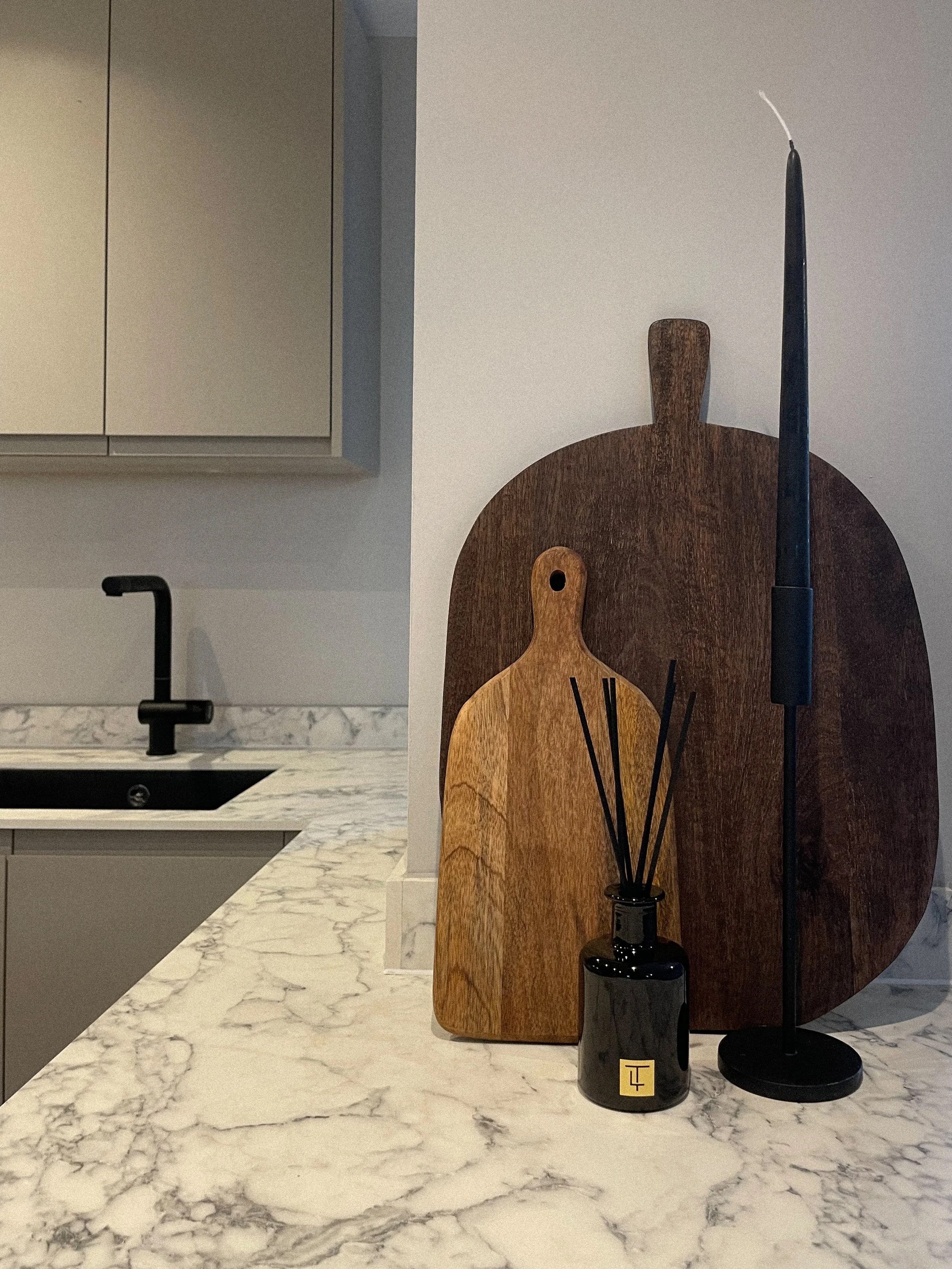 Kitchen countertop with two wooden cutting boards, a black reed diffuser, and a tall black candle holder with a white candle against a white wall.Residential interior design project in Scotland - Interior Designer Scotland - Interiors 