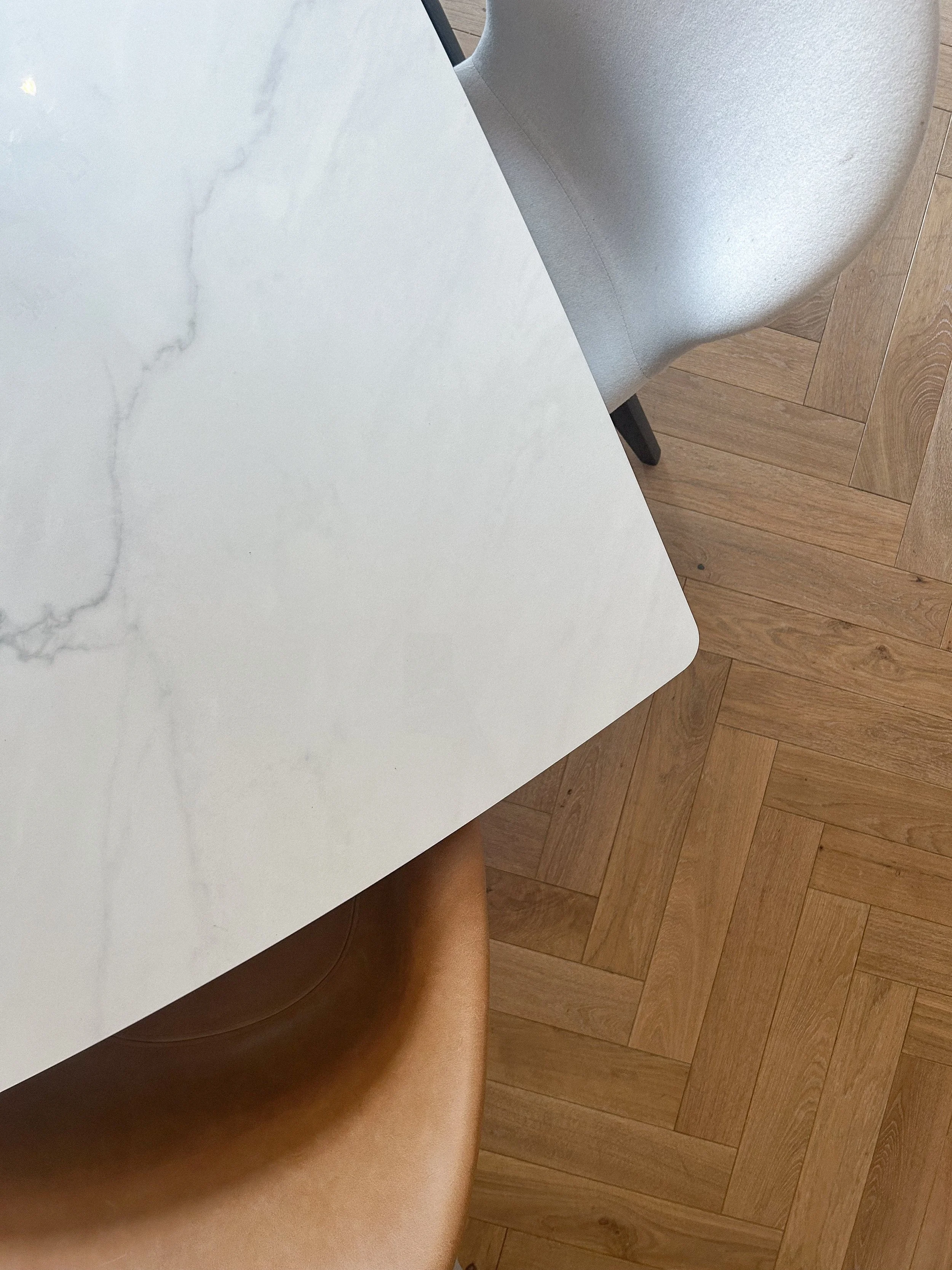 Top-down view of a white marble table, with a beige leather chair at the bottom and a light grey fabric chair at the top right. Wooden floor with a herringbone pattern.Residential interior design project in Scotland - Interior Designer Scotland - Int