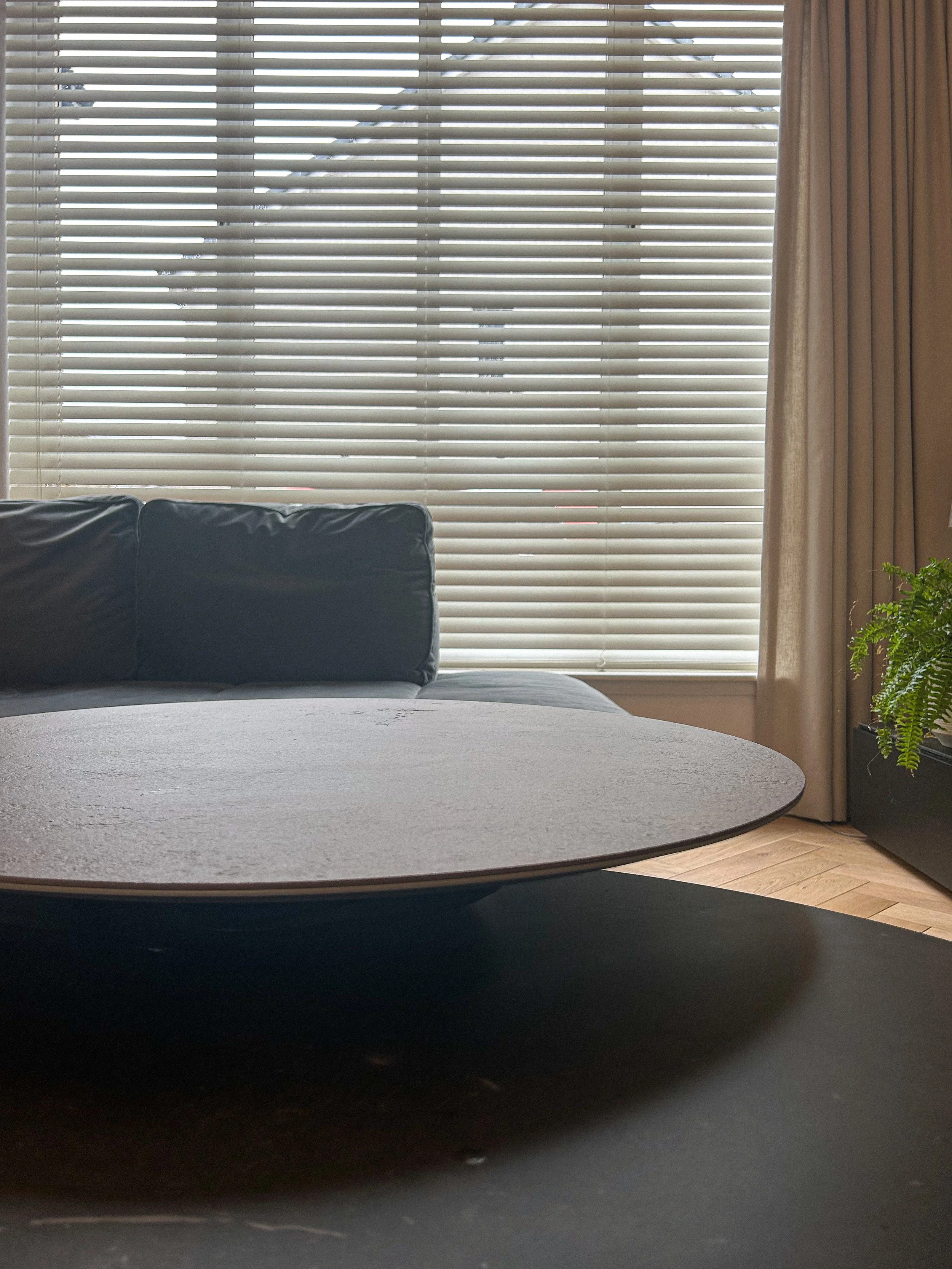 A living room with horizontal blinds on large windows, black leather couch, round coffee table, and a green potted plant.Residential interior design project in Scotland - Interior Designer Scotland - Interiors 