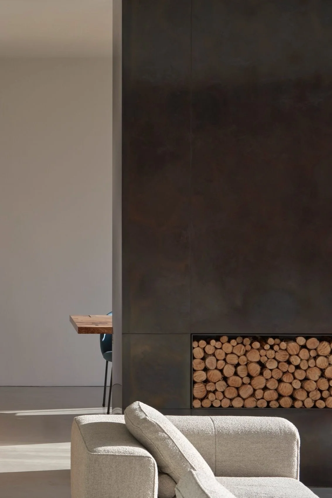 Modern living room featuring a gray couch, a dark wall with a wood log storage, and a small wooden table with a chair in the background.“Residential interior design project in Scotland by [Studio Name], working across Glasgow, Edinburgh, Dundee and t