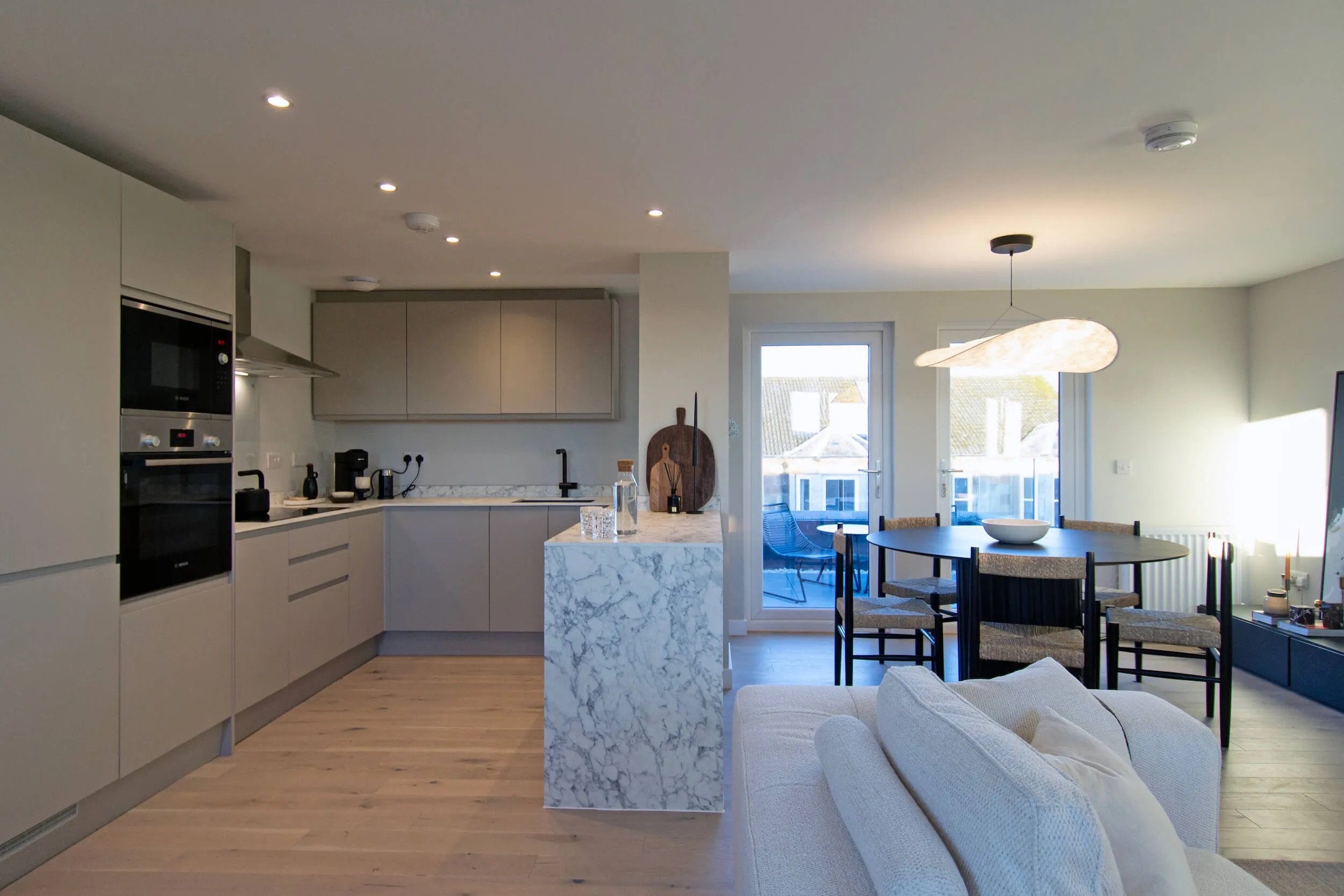 Open-concept kitchen and living room with marble island, dining table, and balcony doors letting in natural light.Residential interior design project in Scotland - Interior Designer Scotland - Interiors 