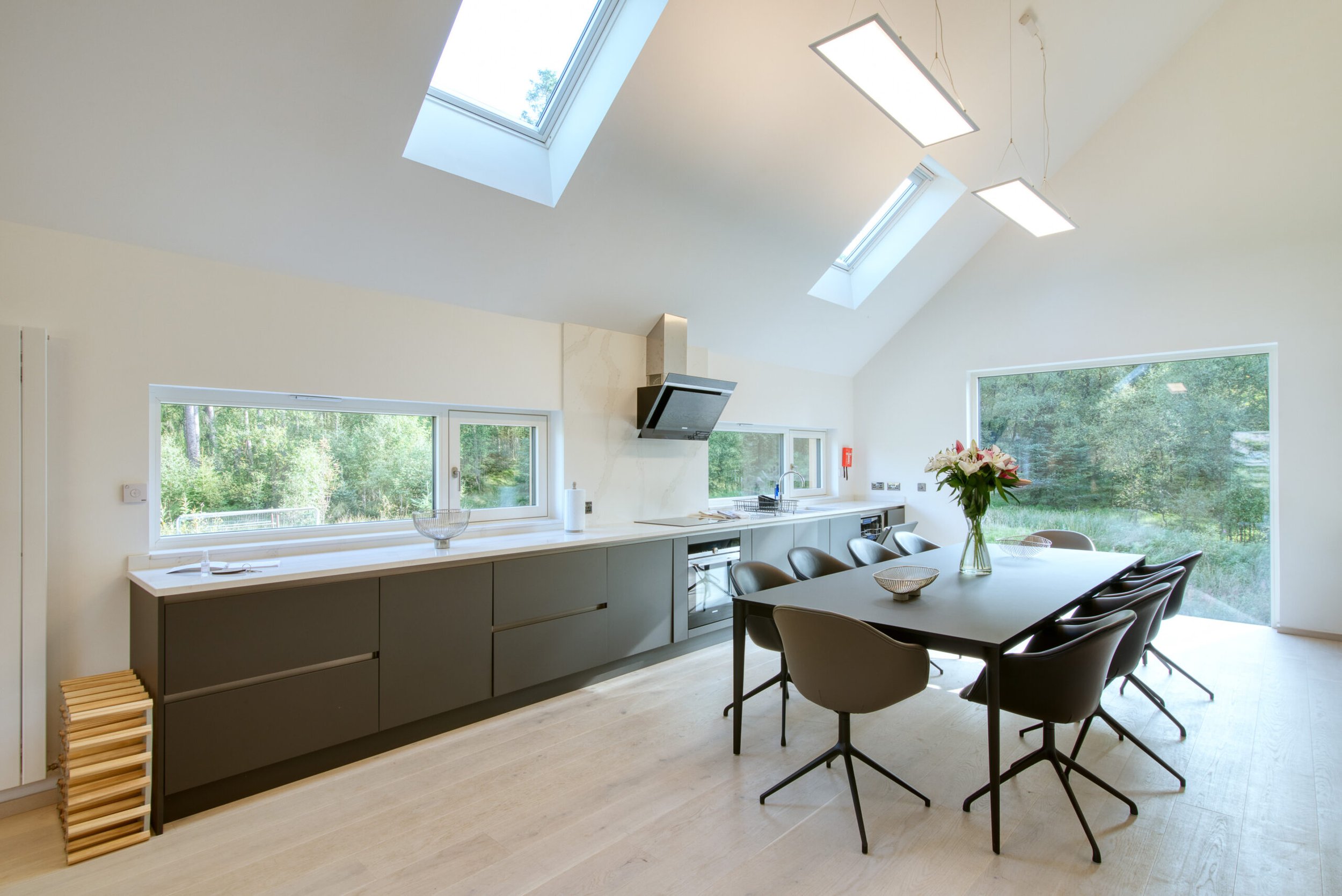 Modern kitchen and dining area with large windows and skylights, black dining table with chairs, kitchen cabinetry, and a vase of flowers.Residential interior design project in Scotland - Interior Designer Scotland - Interiors 