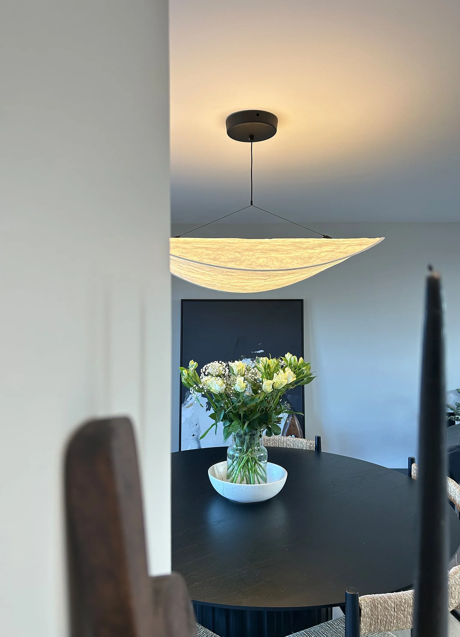 A dining room with a black round table, a white vase with white flowers, a large pendant light, and a television on the wall.Residential interior design project in Scotland - Interior Designer Scotland - Interiors 