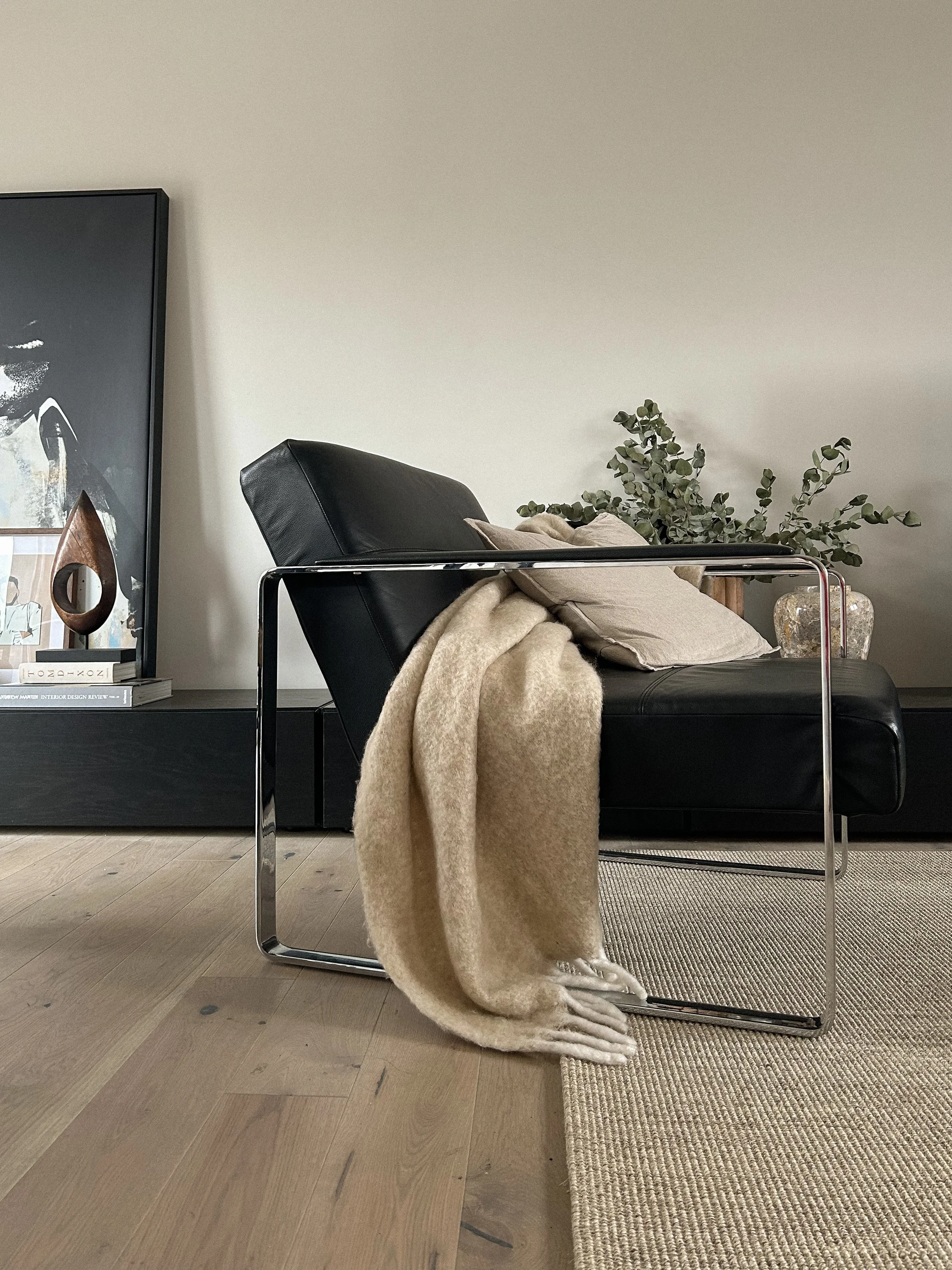 Living room with black leather chair, beige blanket, pillows, green plant, and decorative items on a black shelf.Residential interior design project in Scotland - Interior Designer Scotland - Interiors 