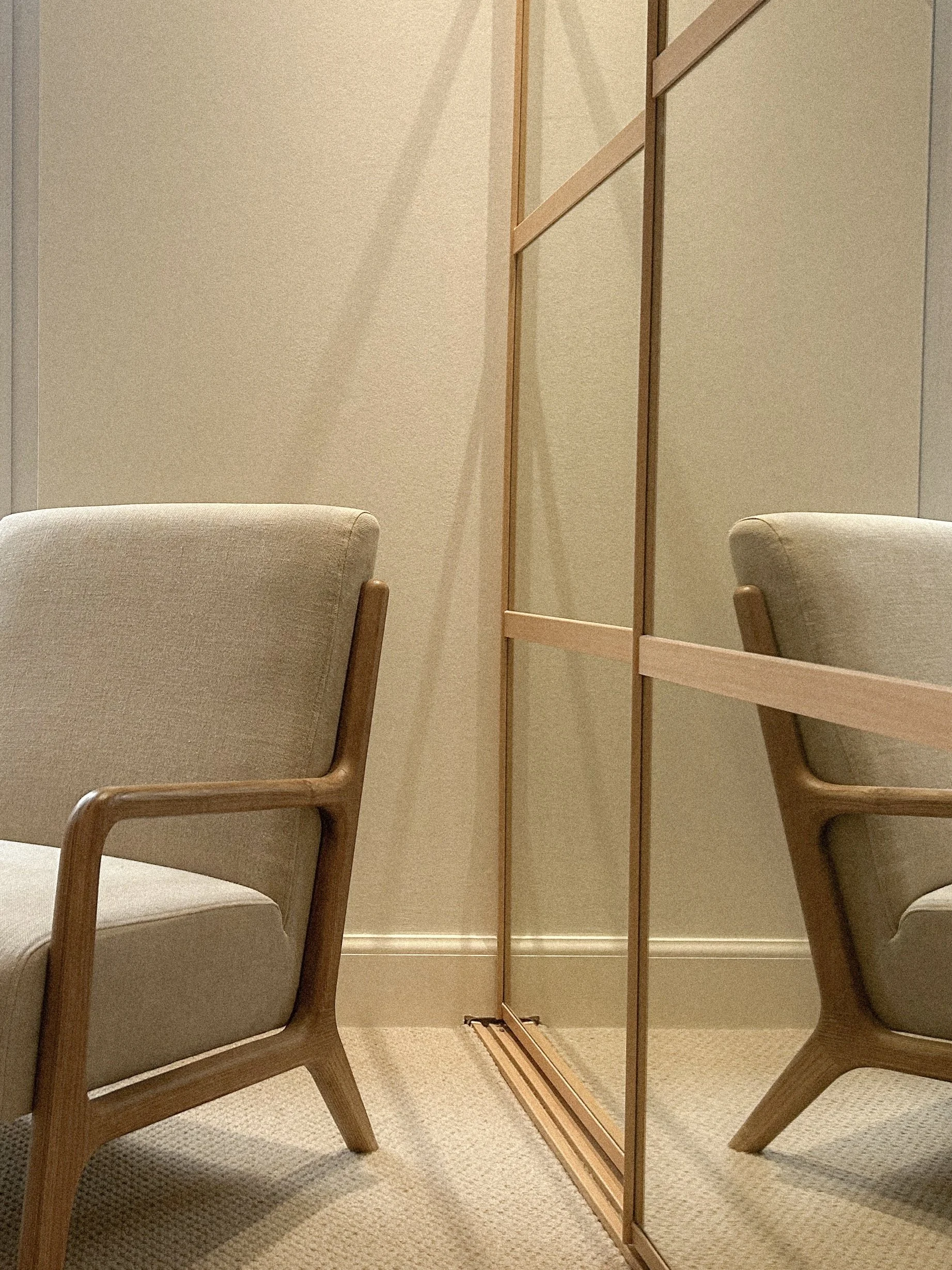 Two beige upholstered chairs with wooden frames sitting on a beige carpet in front of a beige wall with wood trim, and a reflecting mirror on the right side.“Residential interior design project in Scotland by [Studio Name], working across Glasgow, Ed