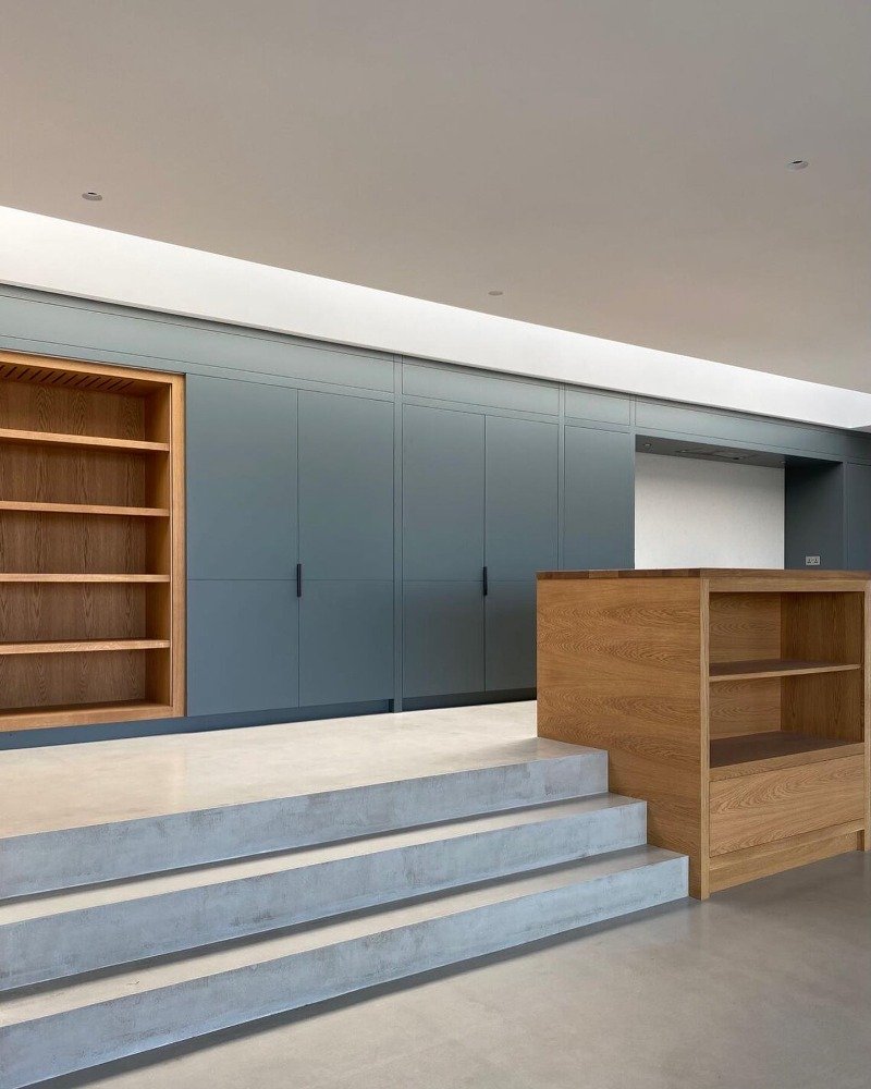 Modern interior space with light gray built-in cabinets, open wooden shelves on a blue wall, a wooden counter or shelf on the right, and concrete steps leading up to the space.“Residential interior design project in Scotland by [Studio Name], working