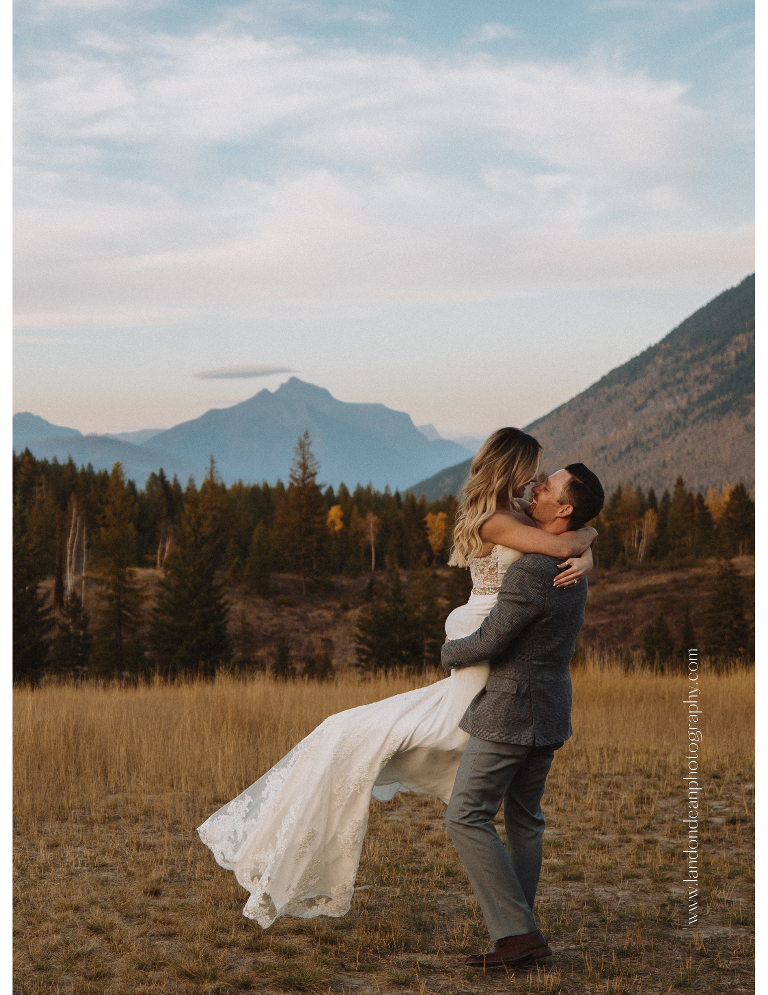 A couple embracing in a field with mountains in the background at sunset in Glacier National Park.