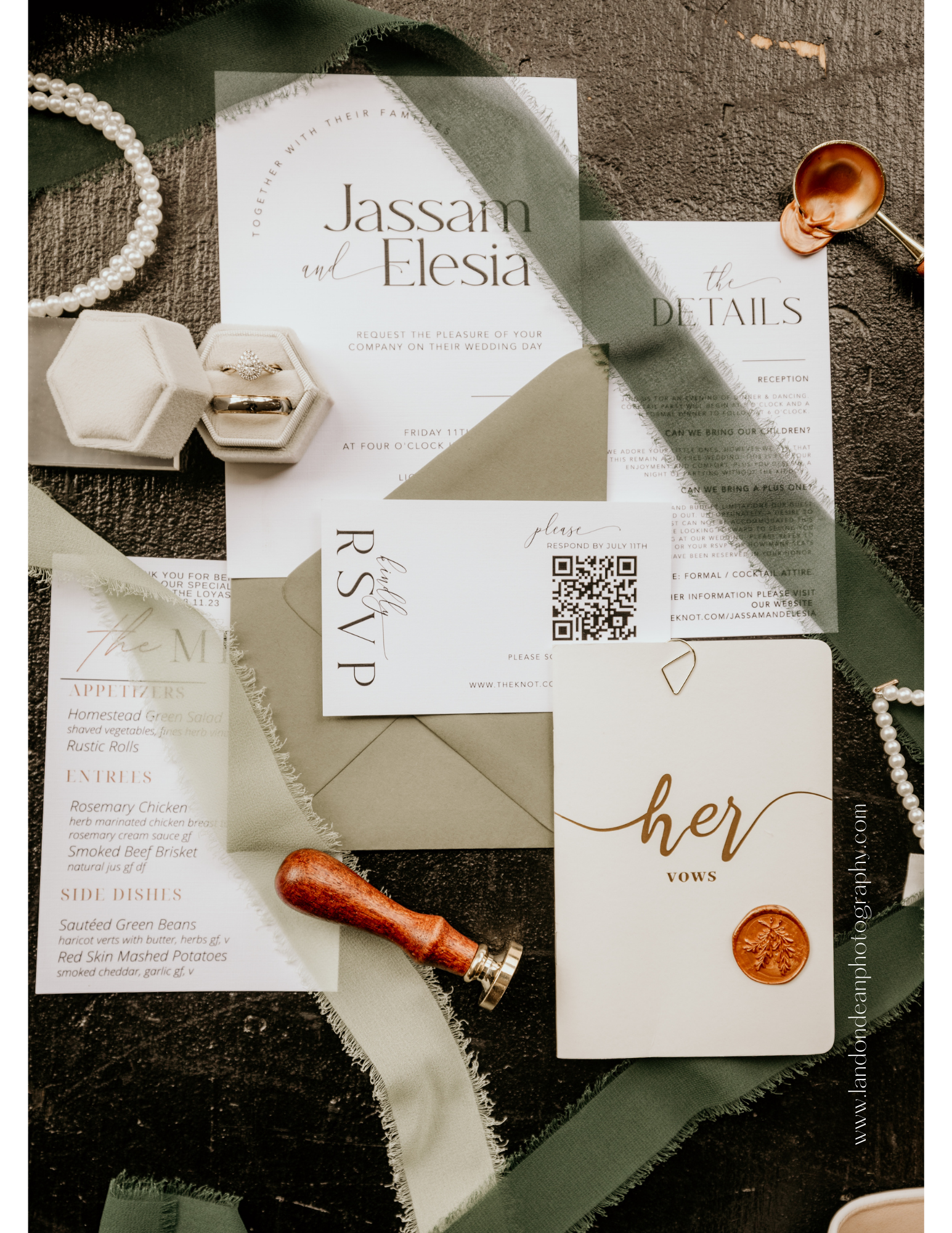 Flat lay of wedding stationery including an invitation, details card, RSVP card, vows booklet, green ribbon, wax seal, and jewelry box with rings on a textured surface.