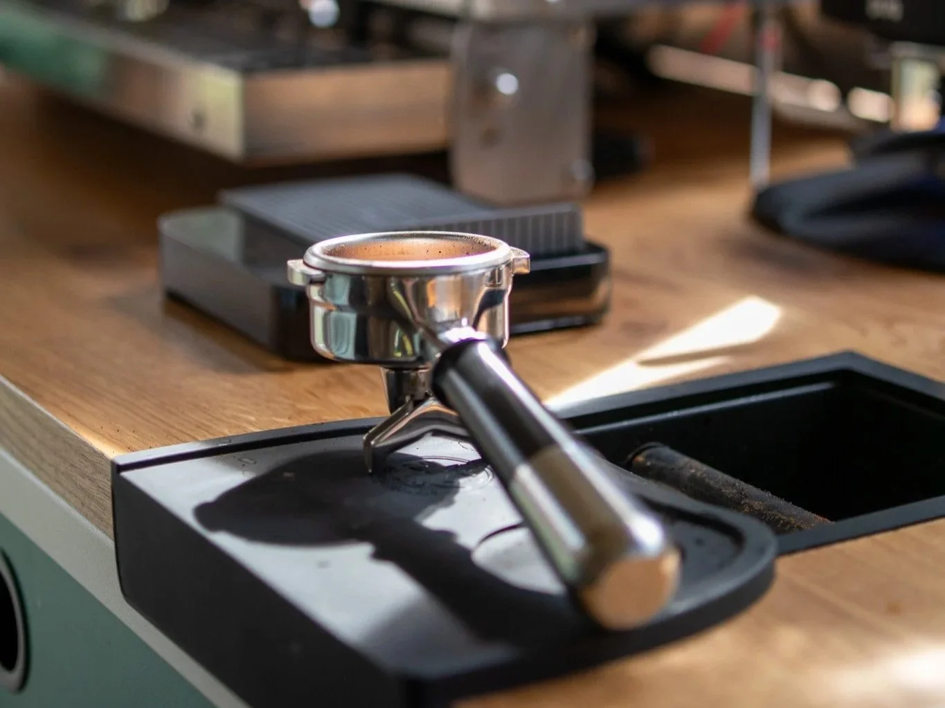 Portafilter klaar om espresso mee te zetten met espressomachine en maler op achtergrond. Synesso, Fiorenzato, Puckpress, Acaia. 