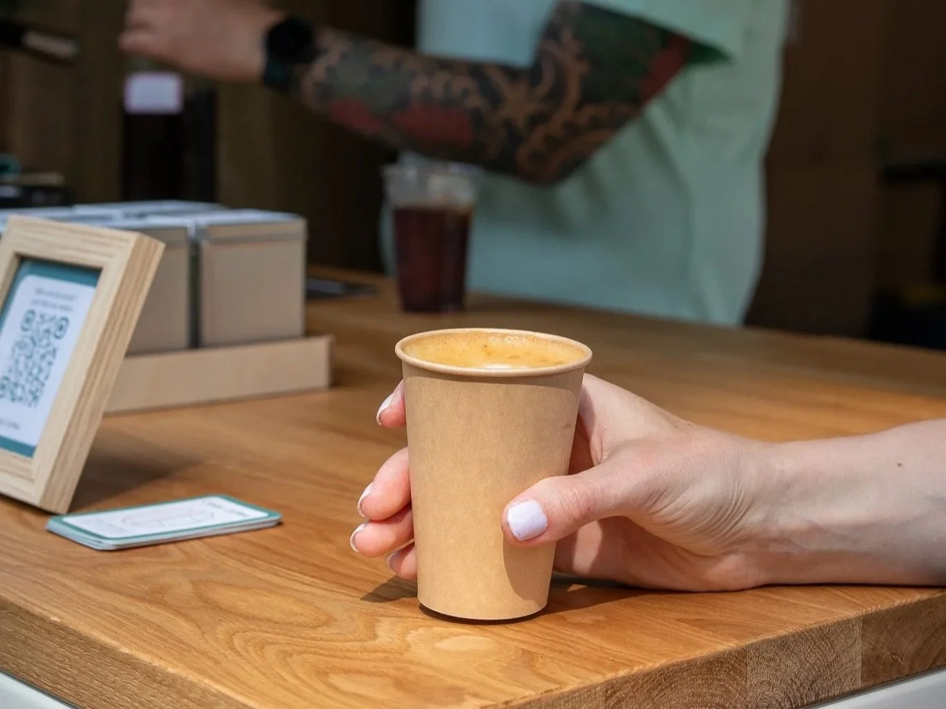 Bezoeker is een cappuccino aan het drinken bij mobiele koffiebar op festival met barista op de achtergrond