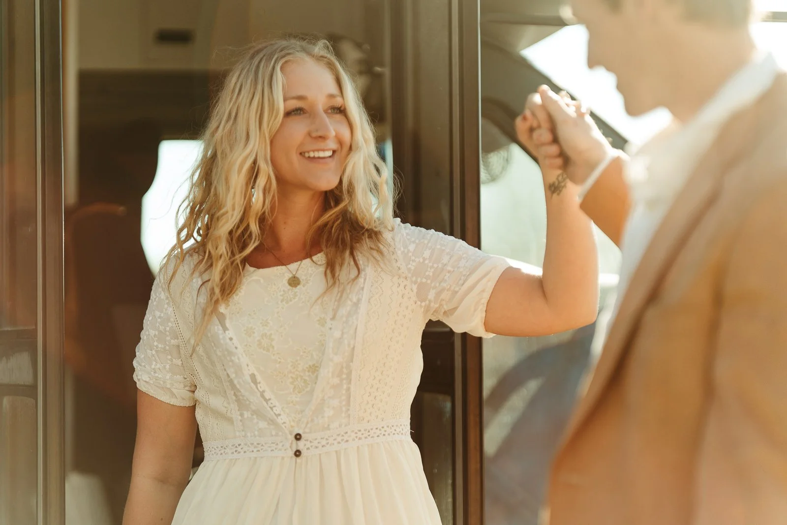 Nikki smiling, looking at Sawyer guiding her out of their skoolie so they can make their way over to their ceremony spot.