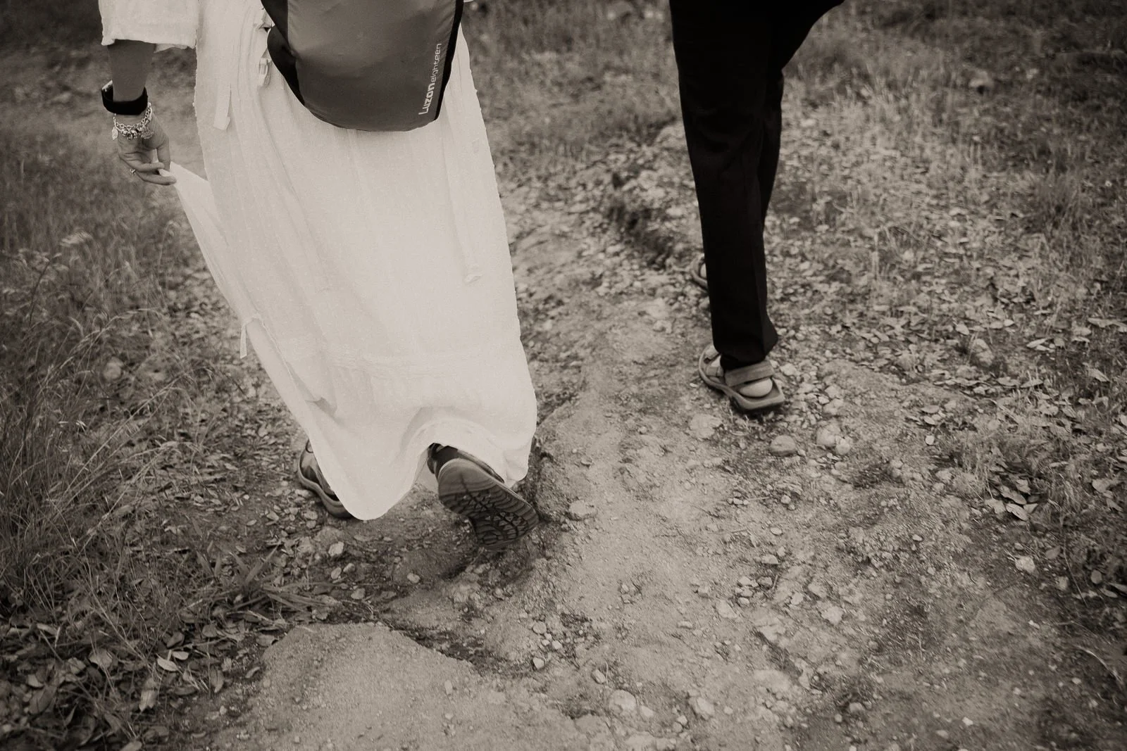 couple’s feet as they walk along a rocky desert trail together