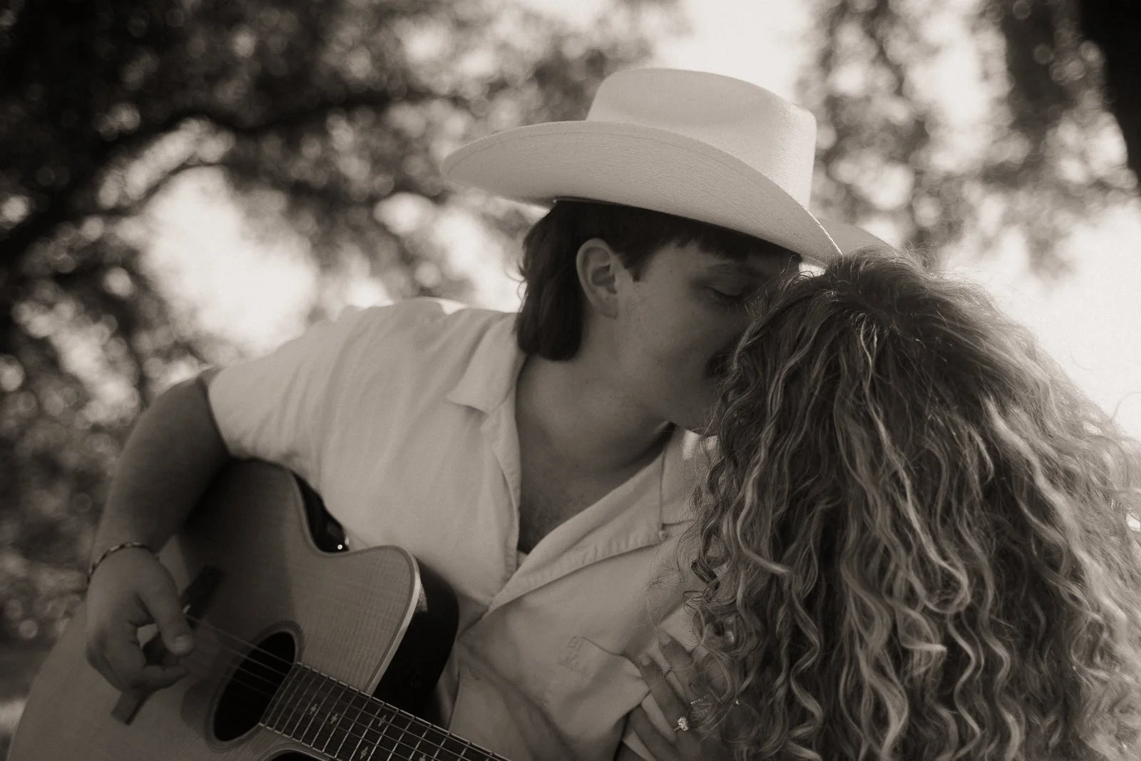 couple kissing while playing the guitar under the trees