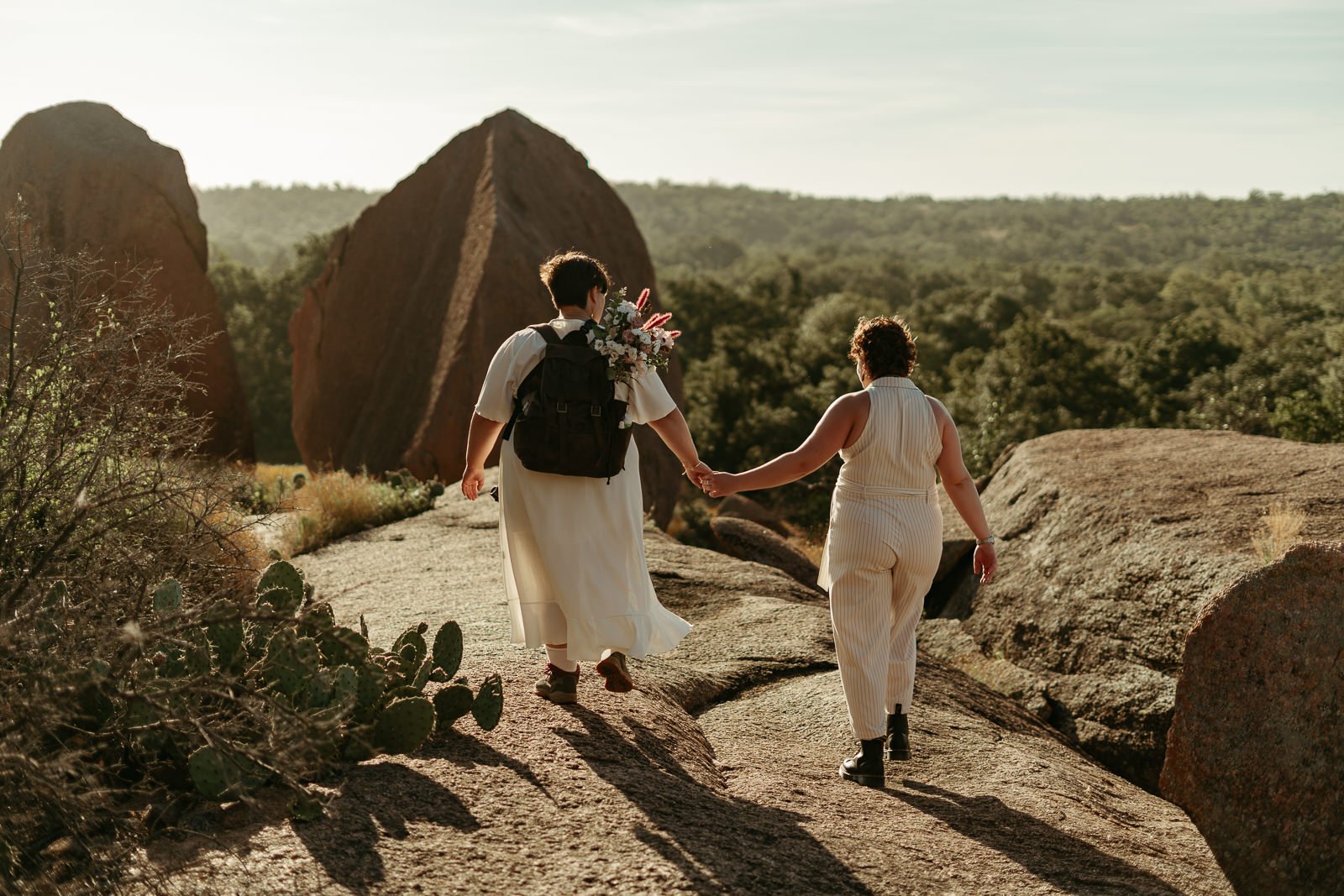 couple holding hands while walking away on boulder at Enchanted Rock in the golden morning light