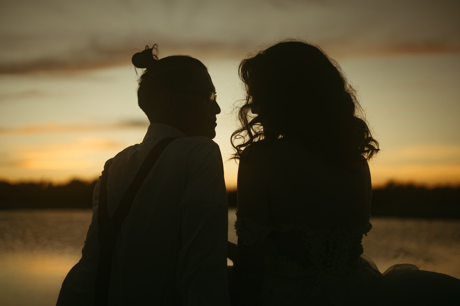 silhouette of a couple sitting by a lake at sunset