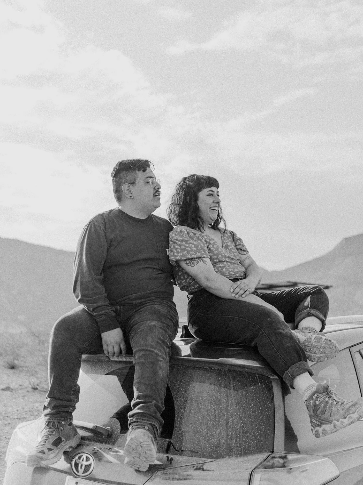 Kevin and Nora, photographer and videographer duo, smiling as they sit on the roof of their dusty RAV4.
