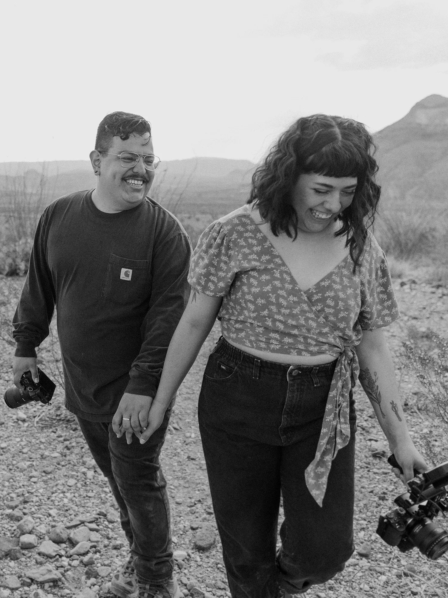 Kevin and Nora elopement photographer and videographer duo walking through the West Texas desert holding their cameras.