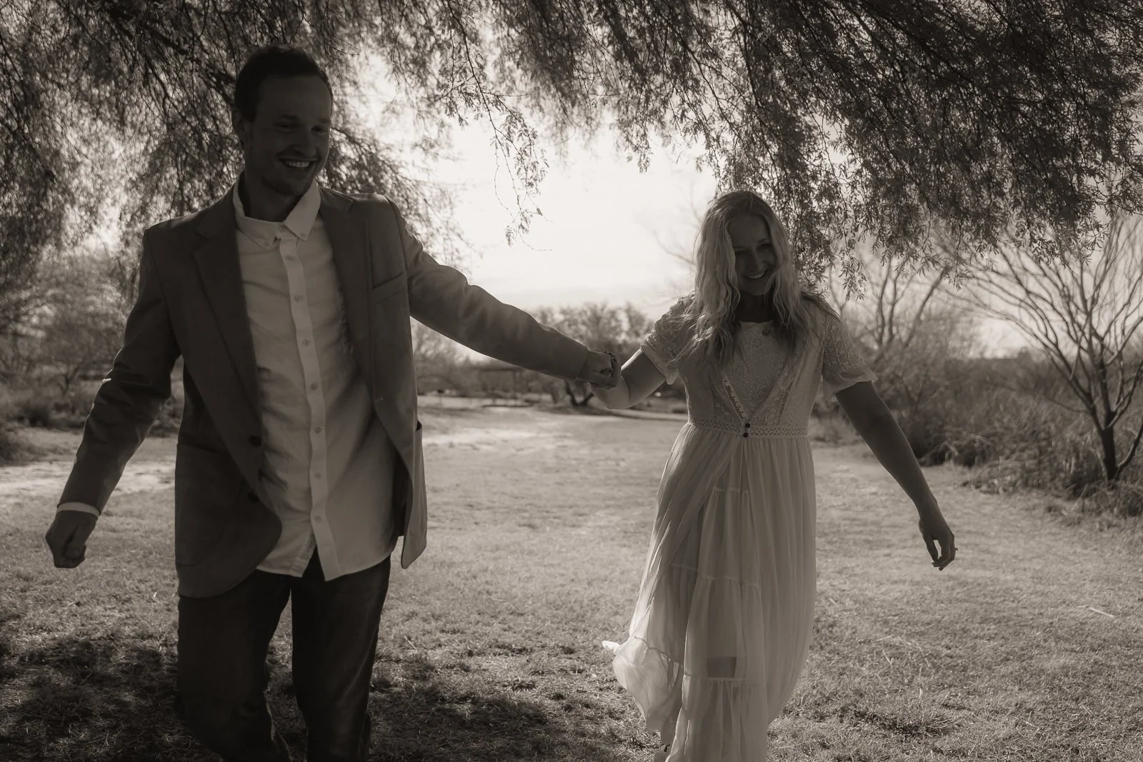 Sawyer and Nikki laugh as they hold hands and run under the huisache together.