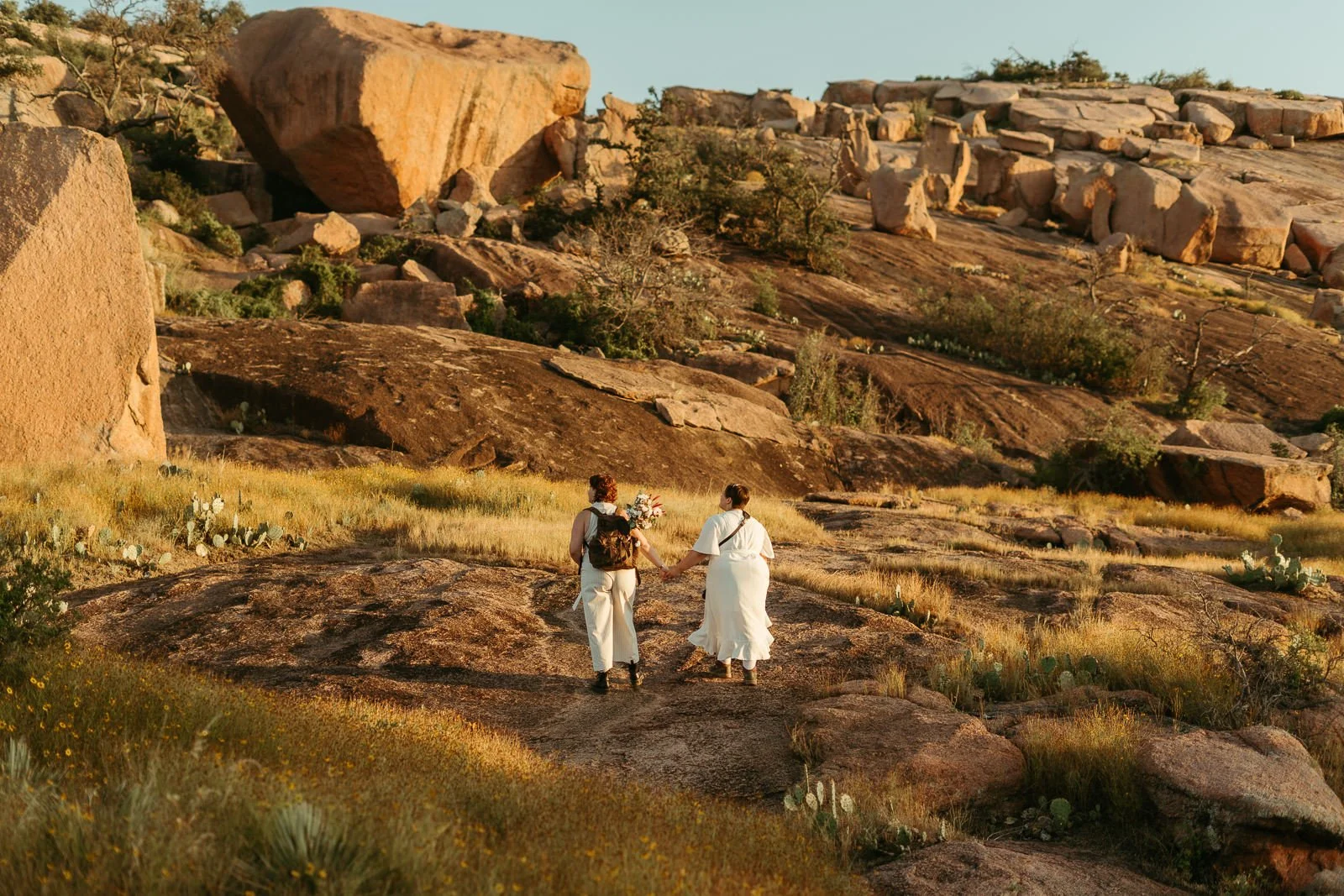 couple holding hands while hiking up a boulder at Enchanted Rock in the golden morning light