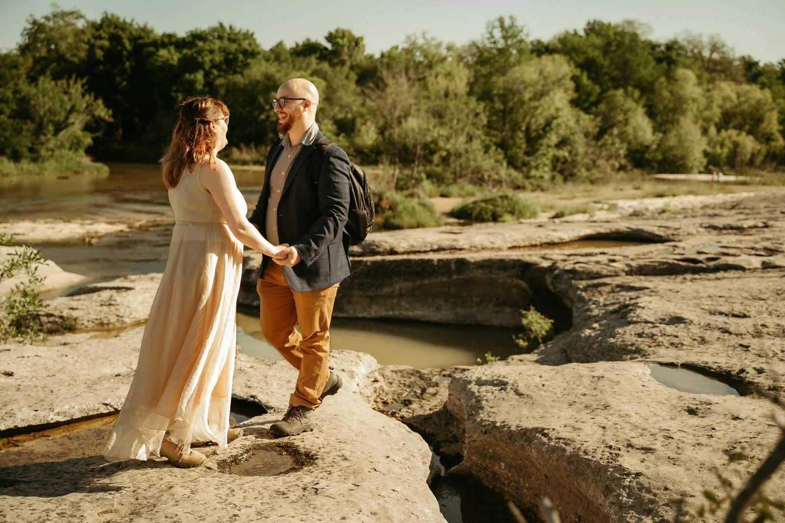 bride and groom laughing while they hold each other's hands near a big vernal pool that is cut into the limestone