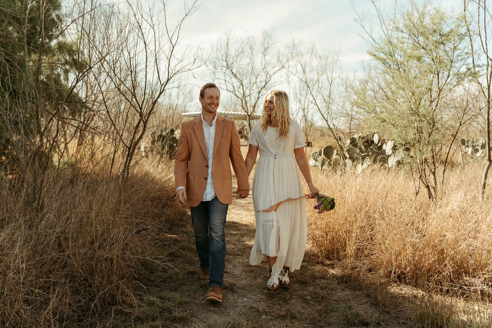 Sawyer and Nikki smiling as they walk into a desert-lined picnic area near their campsite for their ceremony.