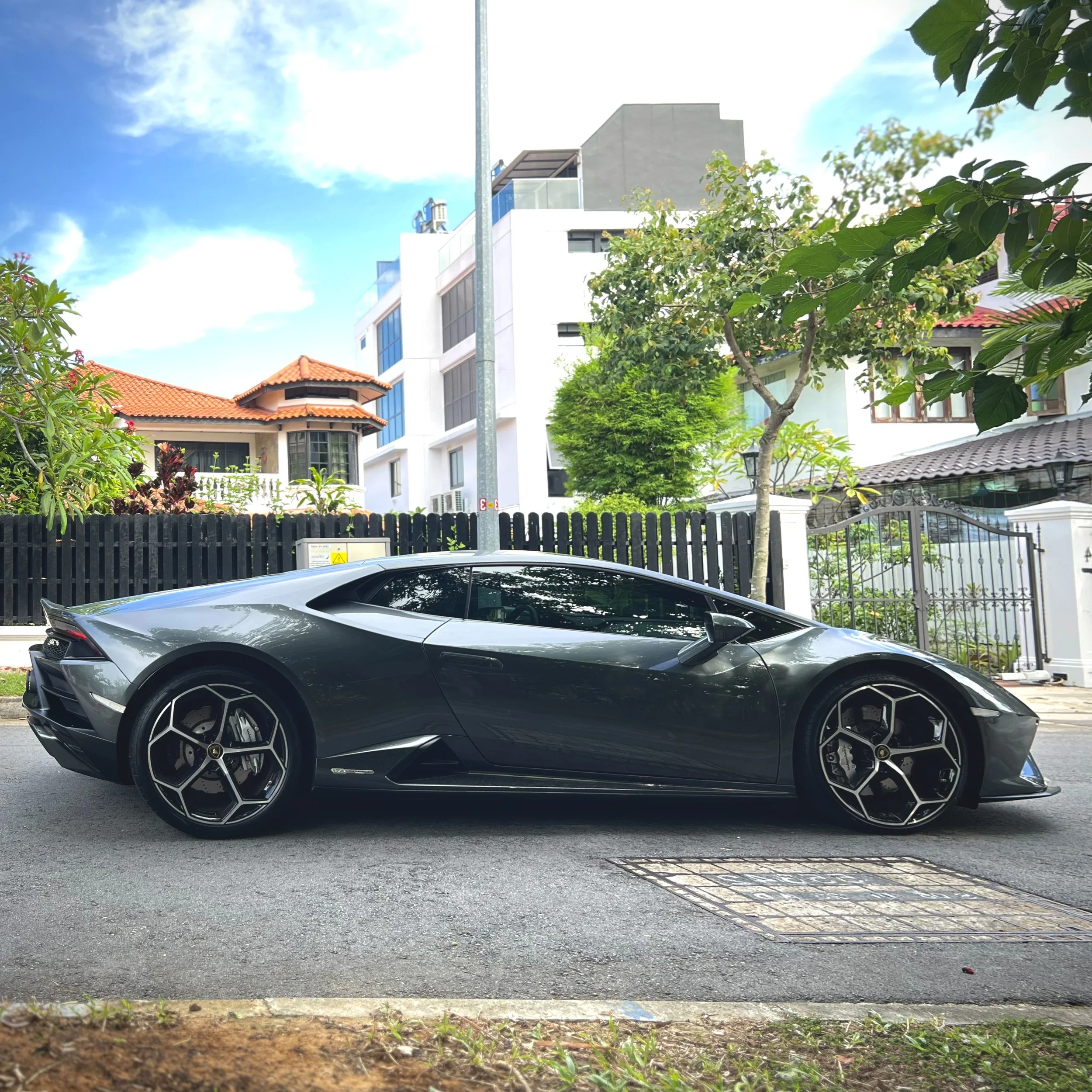 Gray sports car parked on a residential street with houses and trees in the background.