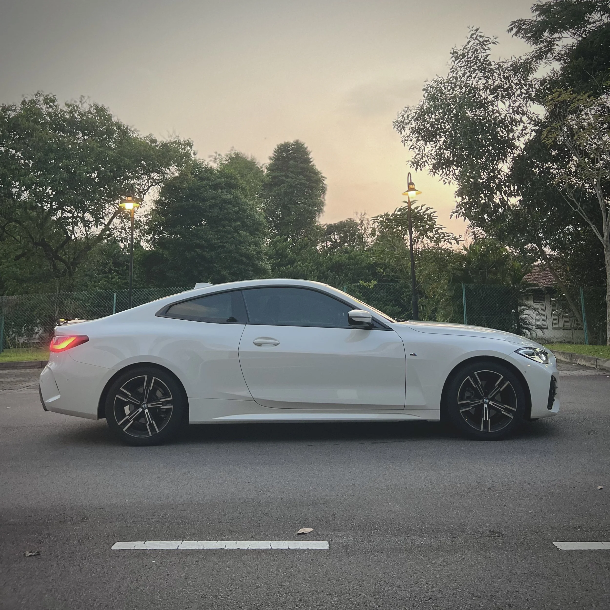 White sports car parked on a road with trees in the background.