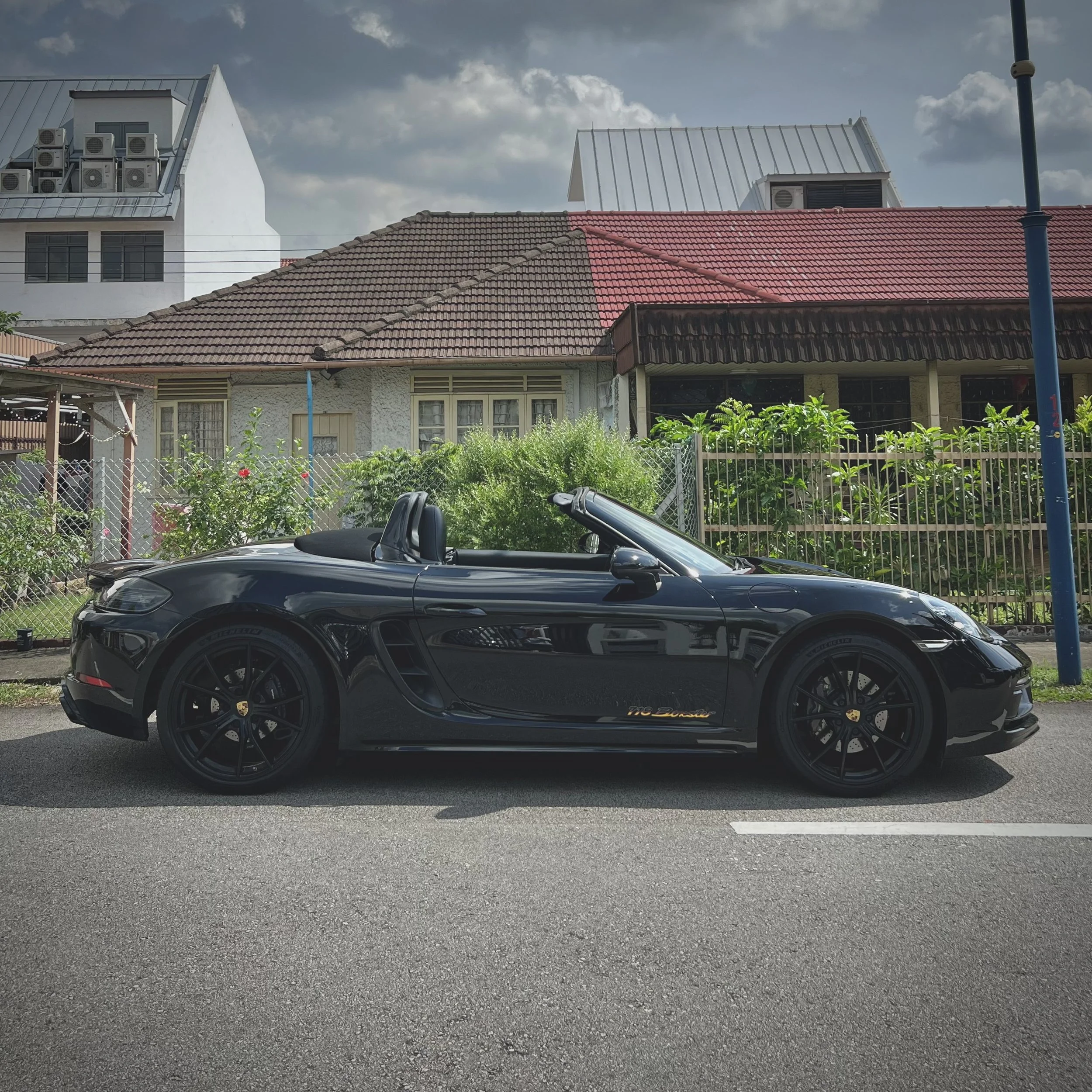 Black convertible sports car parked on a residential street with houses in the background.